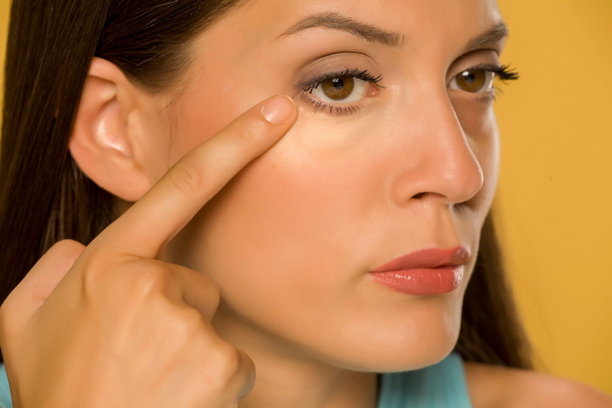 黄色の背景に彼女の低まぶたに触れる若い女性