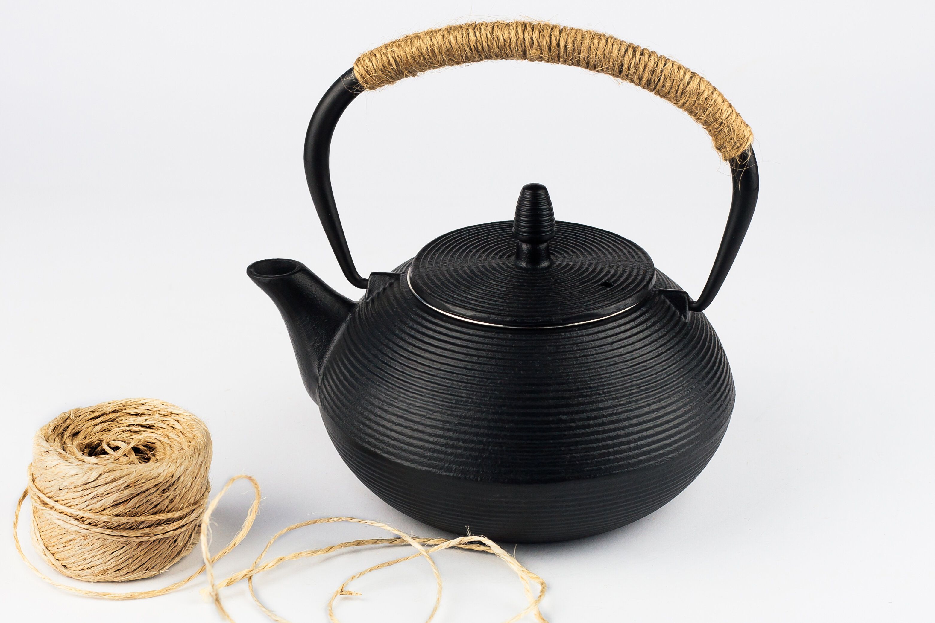 ハンドルにロープと白い背景にロープのスケインと黒のティーポットのクローズアップ