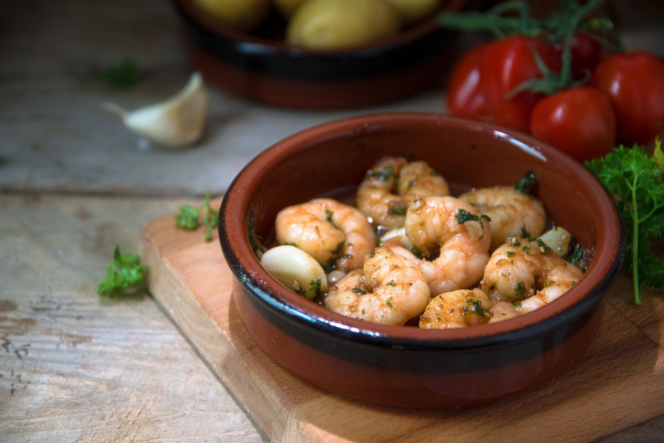 エビやニンニクでエビとタパス ボウル、木の板、ジャガイモ、トマト、素朴なスタイルは暗い背景にハーブのスペイン前菜のオリーブ オイル