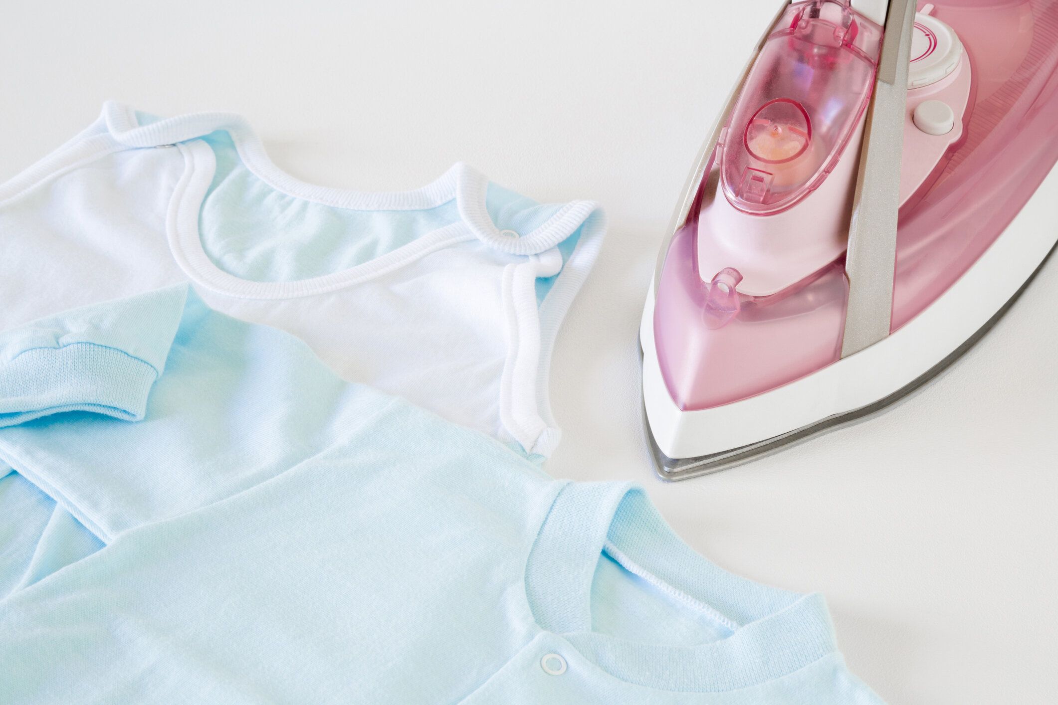 ホワイト ボードに青いボディー スーツを光にきれいで、しわアイロン。赤ちゃんの服を気に。母の義務。毎日のルーチン。ピンクでモダンな電気アイロンとスチーム システム。