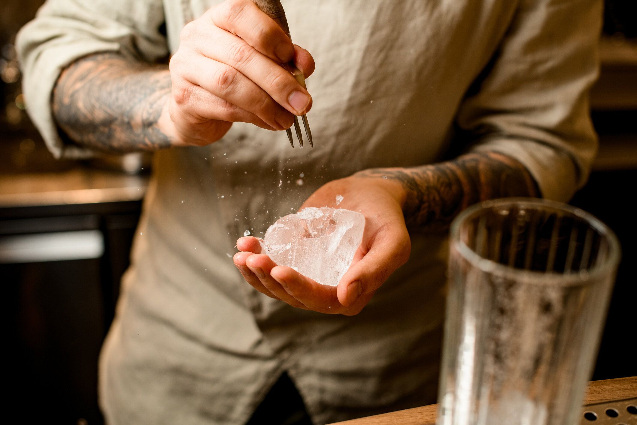 バーテンダーは手に氷の一部を保持し、金属トライデントでそれを壊します。