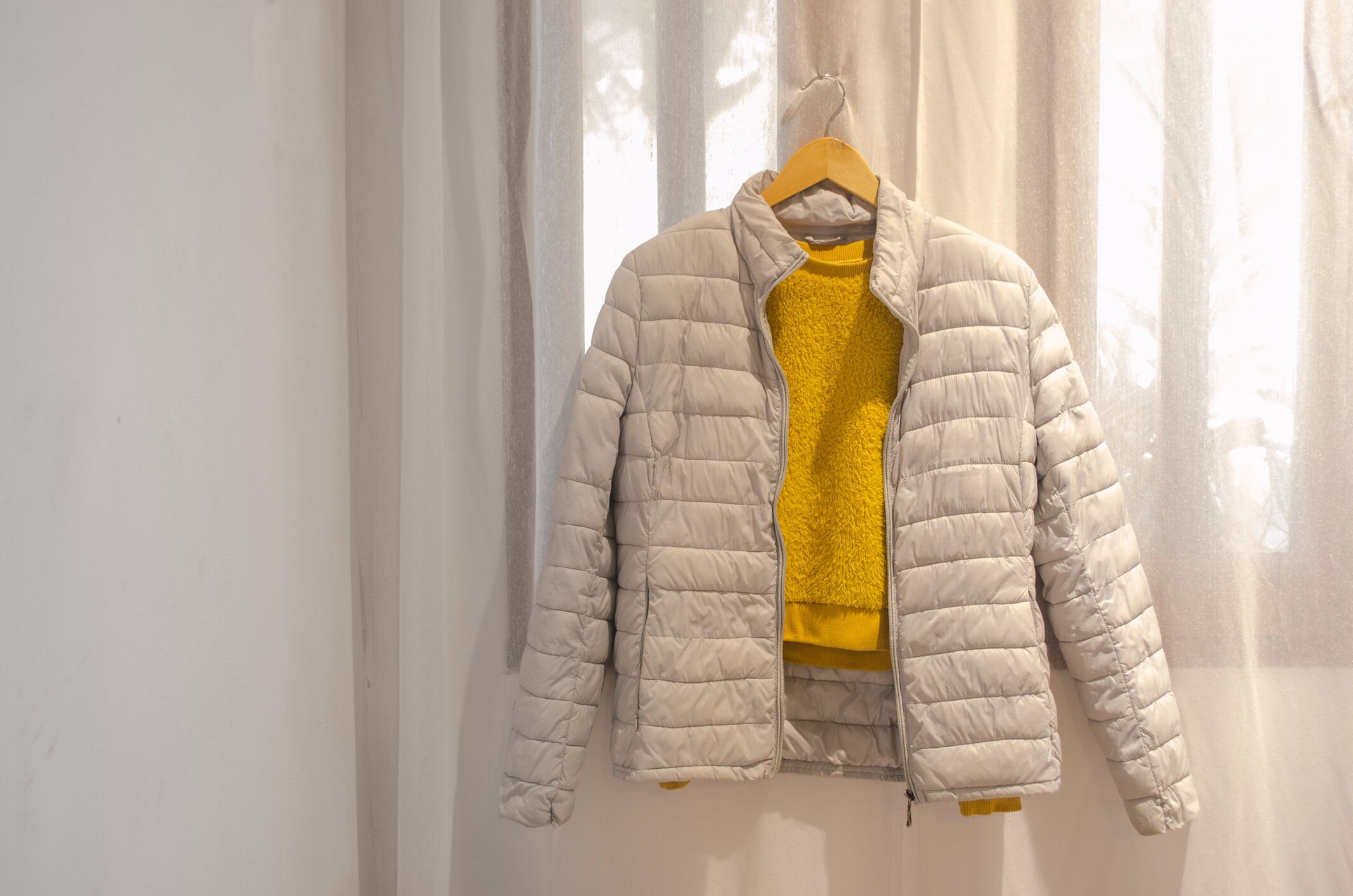 明るい背景に木製のハンガーにぶら下がっている灰色のジャケットと黄色のセーター。トレンディな色の服。