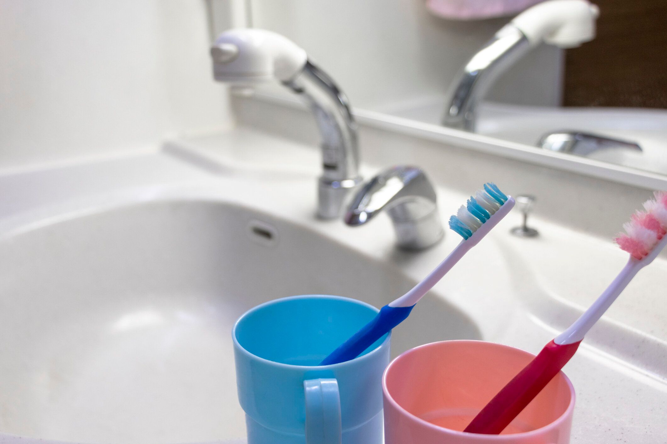 白い洗面台にカラフルなカップと歯ブラシ
