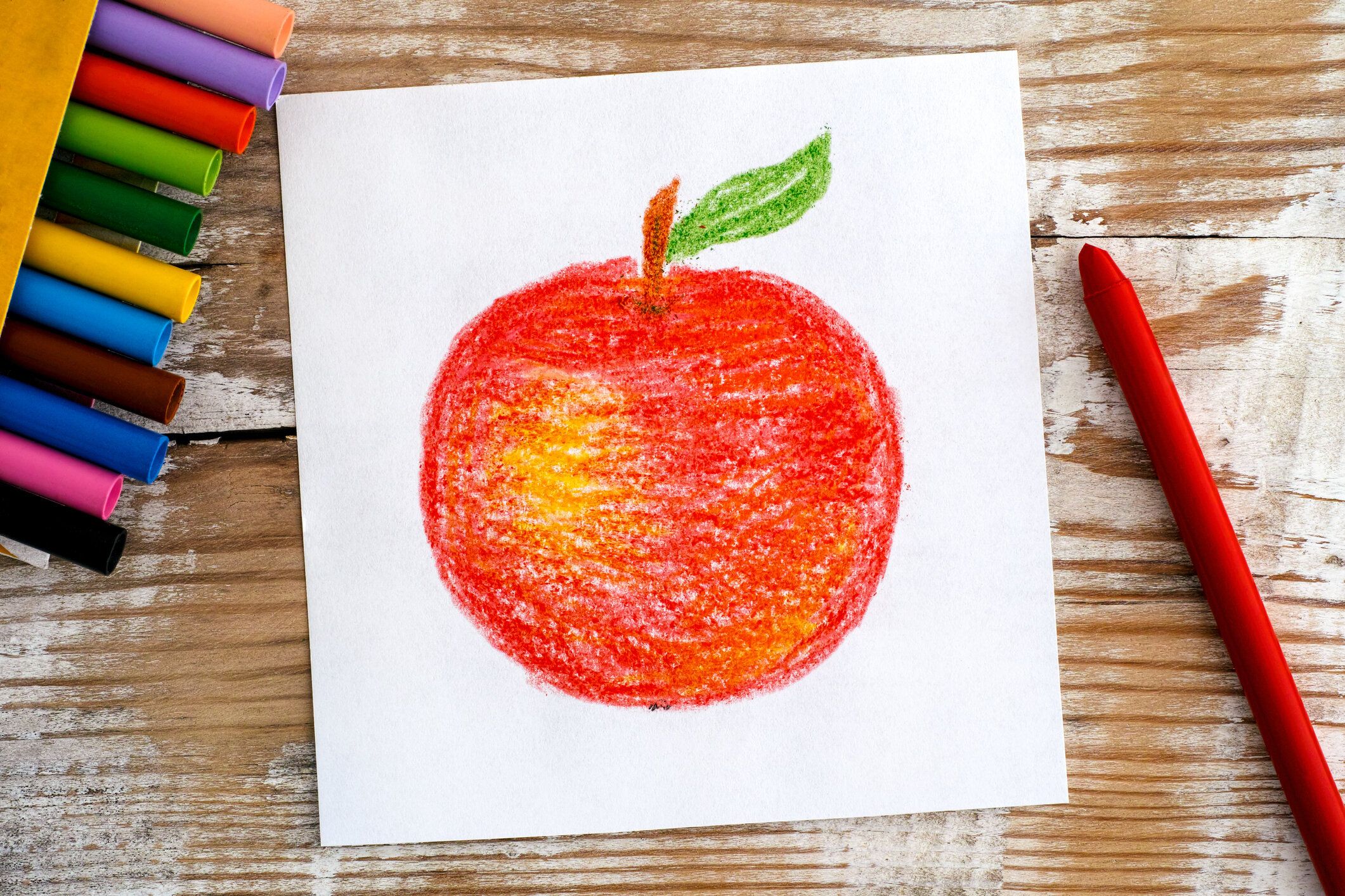 ワックスクレヨンと手描きレッドアップル。木製の背景。