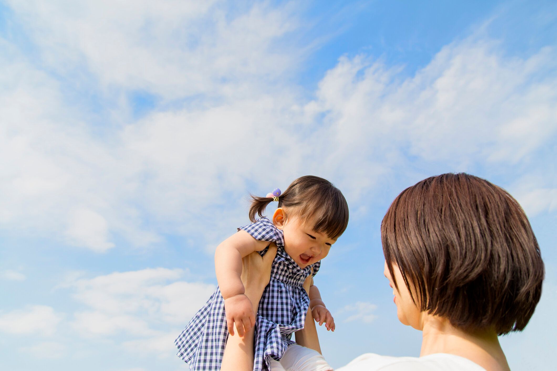 青空に対して高い娘に持ち上げる母