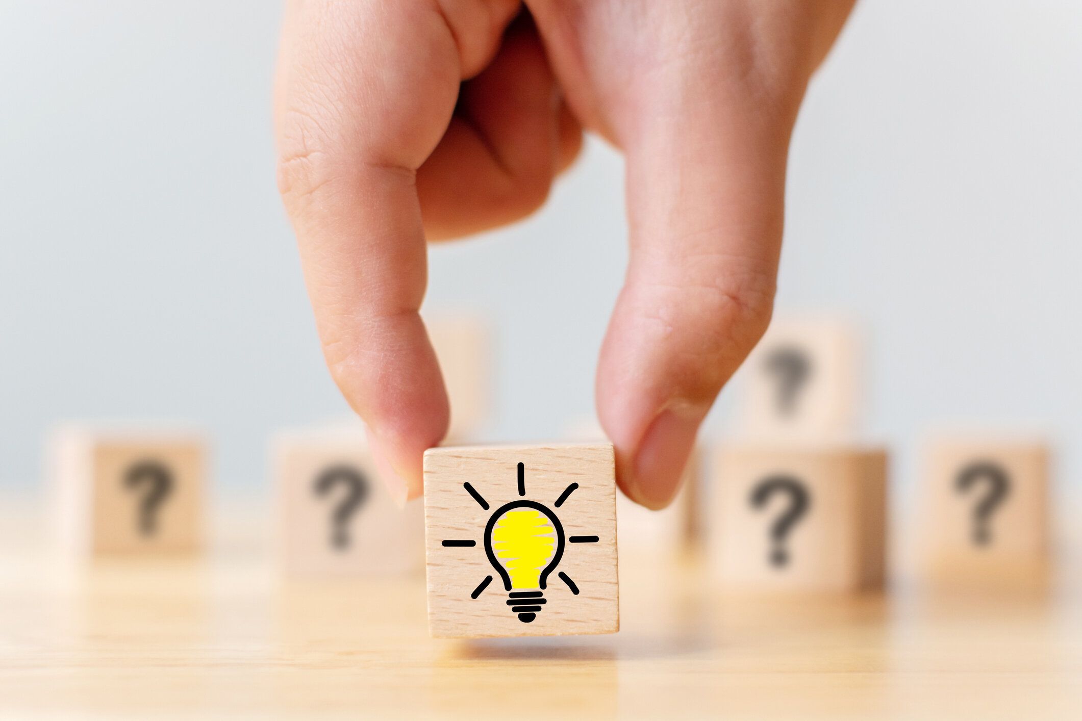 コンセプト創造的なアイデアと革新。手は疑問符記号と電球アイコンで木の立方体のブロックを選んだ