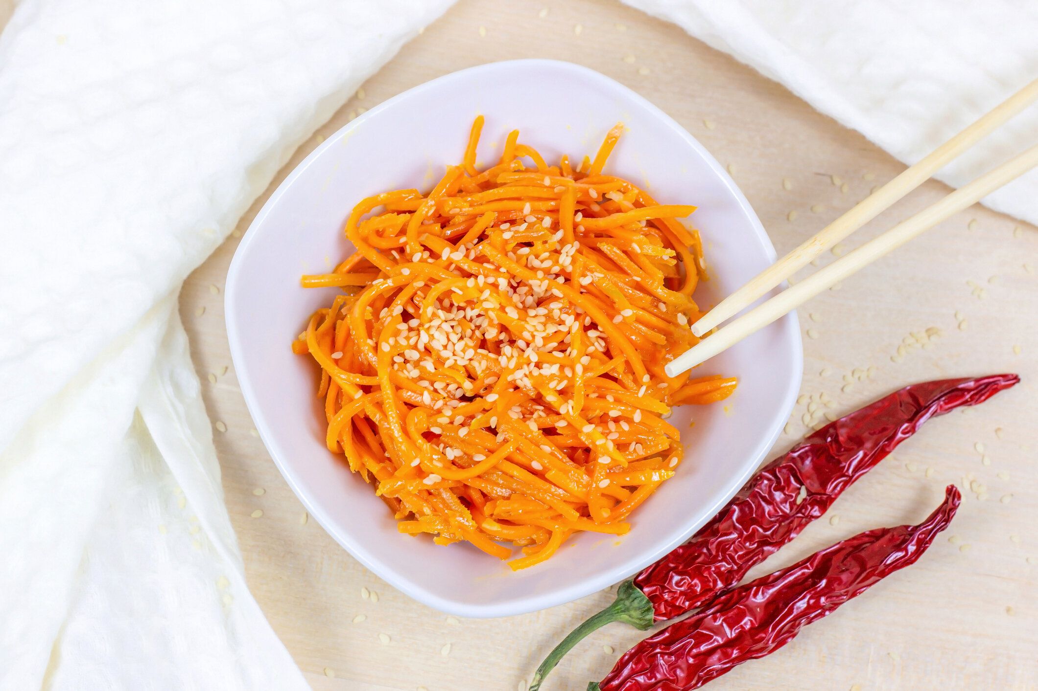 明るい背景に白いボウルでスパイシーな韓国ニンジンサラダのトップビュー