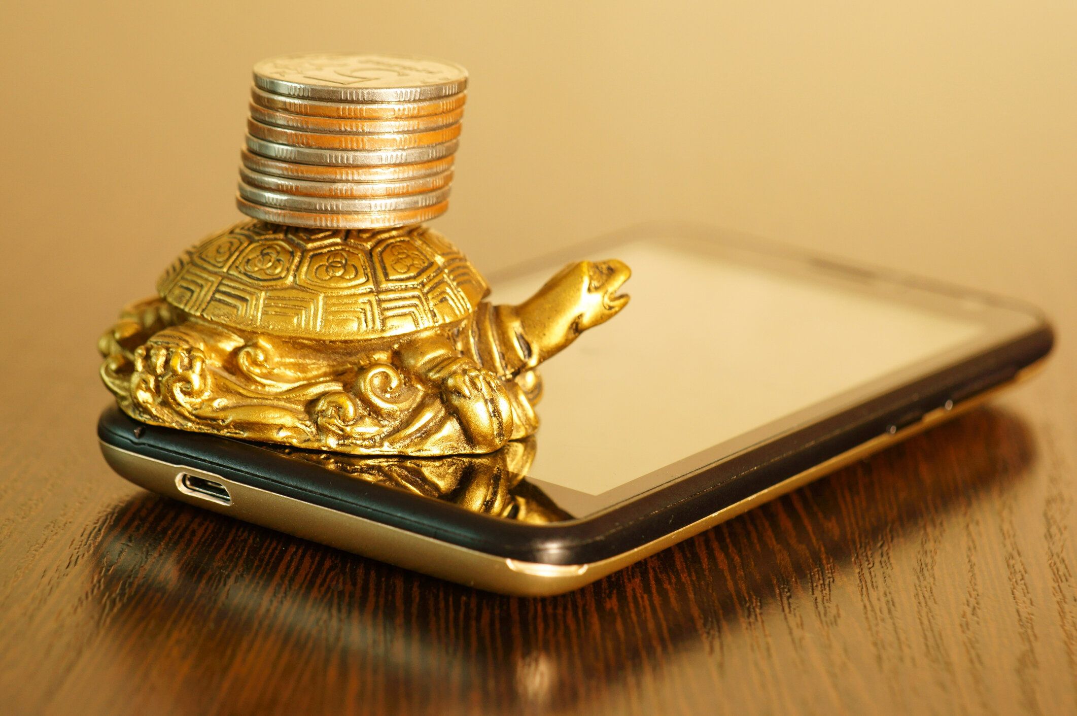 スマートフォンにコインを持つ金属カメ。