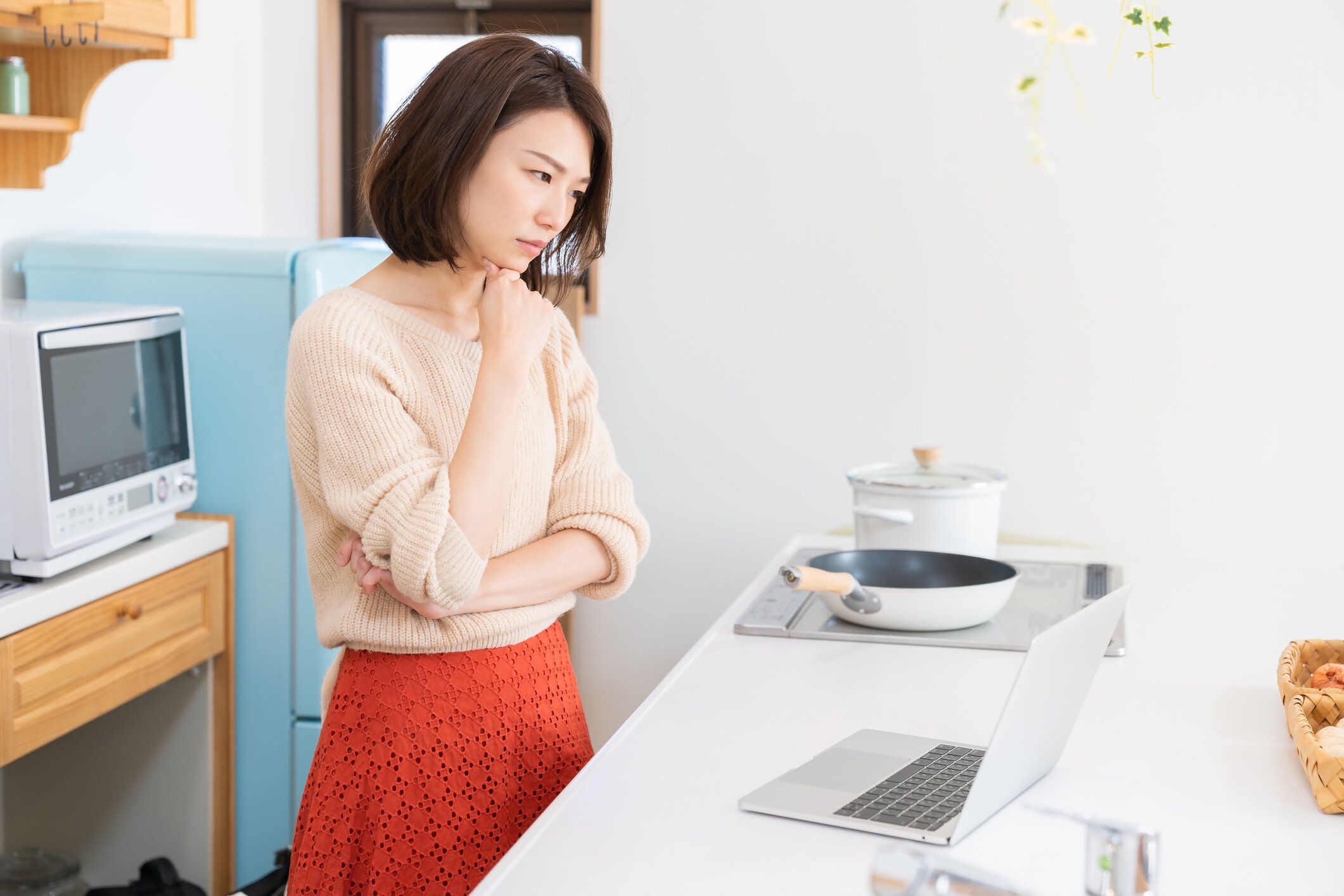 ラップトップ、キッチンを使用して若いアジアの女性は、考え、