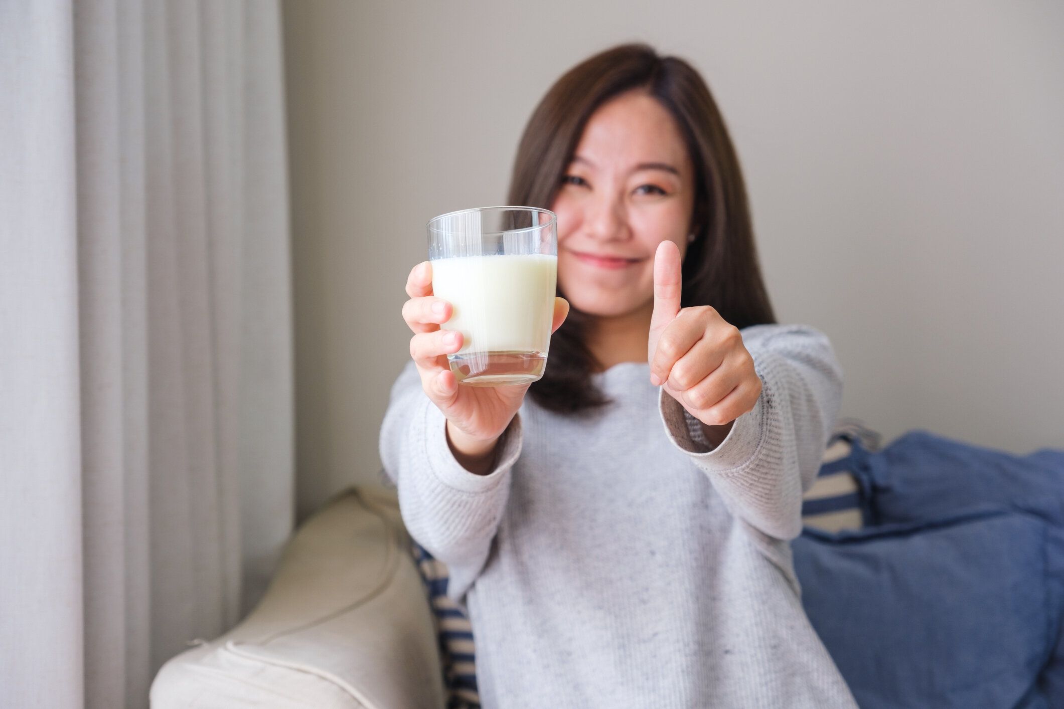 新鮮な牛乳のグラスを持ちながら親指を立ててハンドサインをする若い女性のポートレート画像