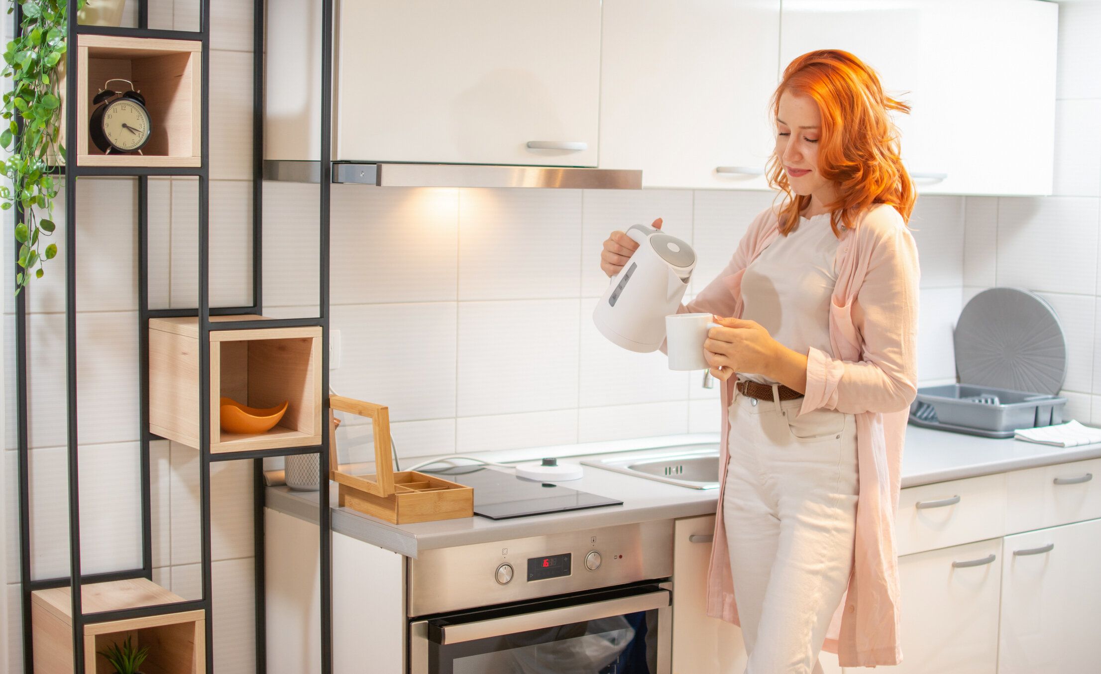 自宅の台所で電気ケトルでお茶を作る若い幸せな生姜の女性。