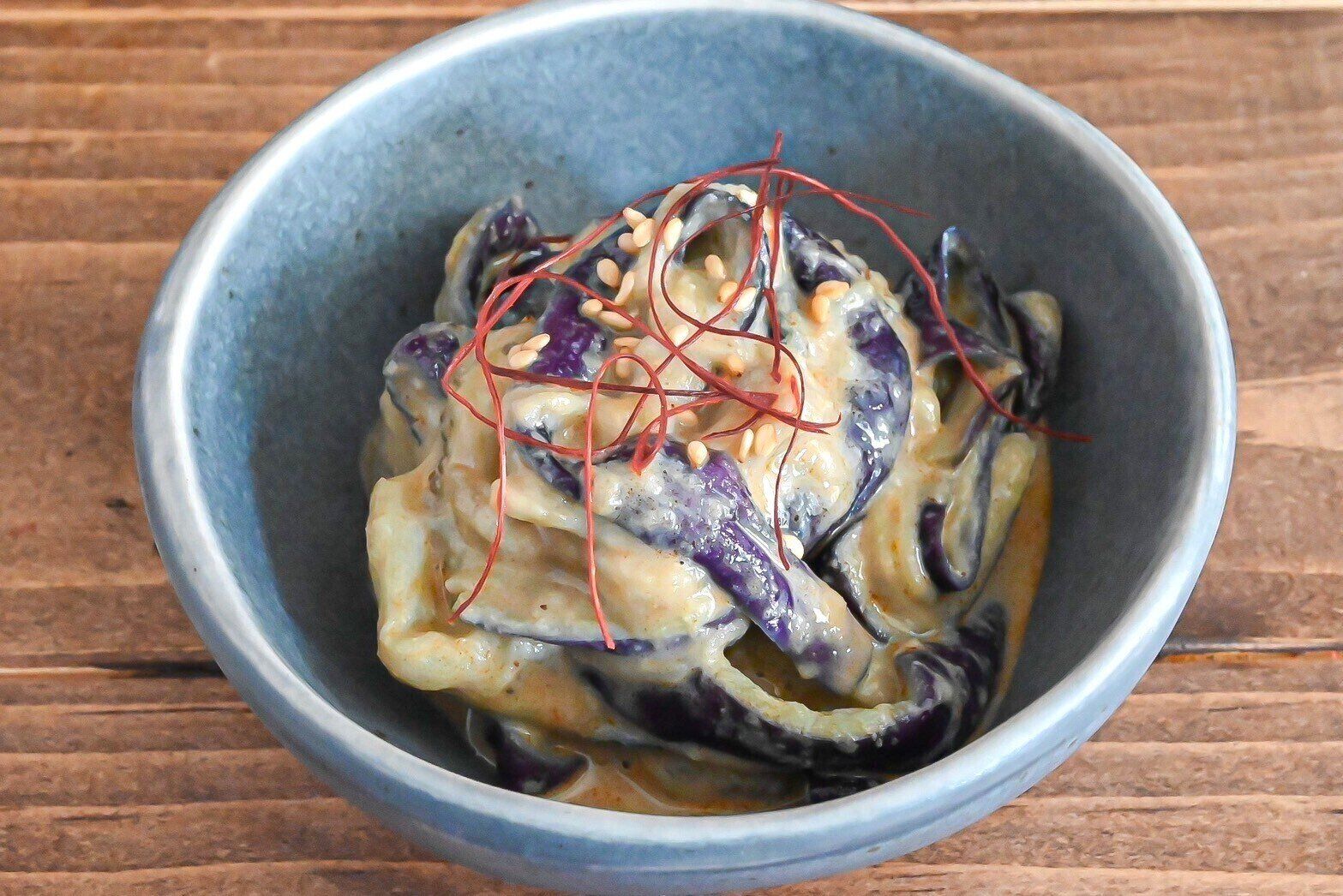 青い皿に盛られた蒸しなすのごま和え