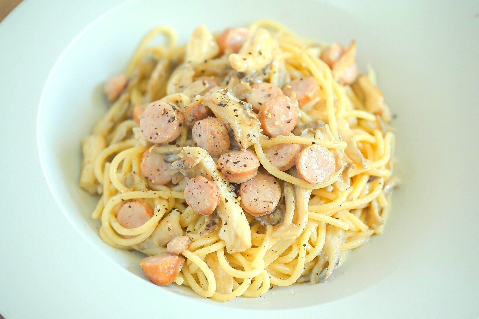 白い皿に盛られたソーセージととまいたけのトリュフクリームパスタ