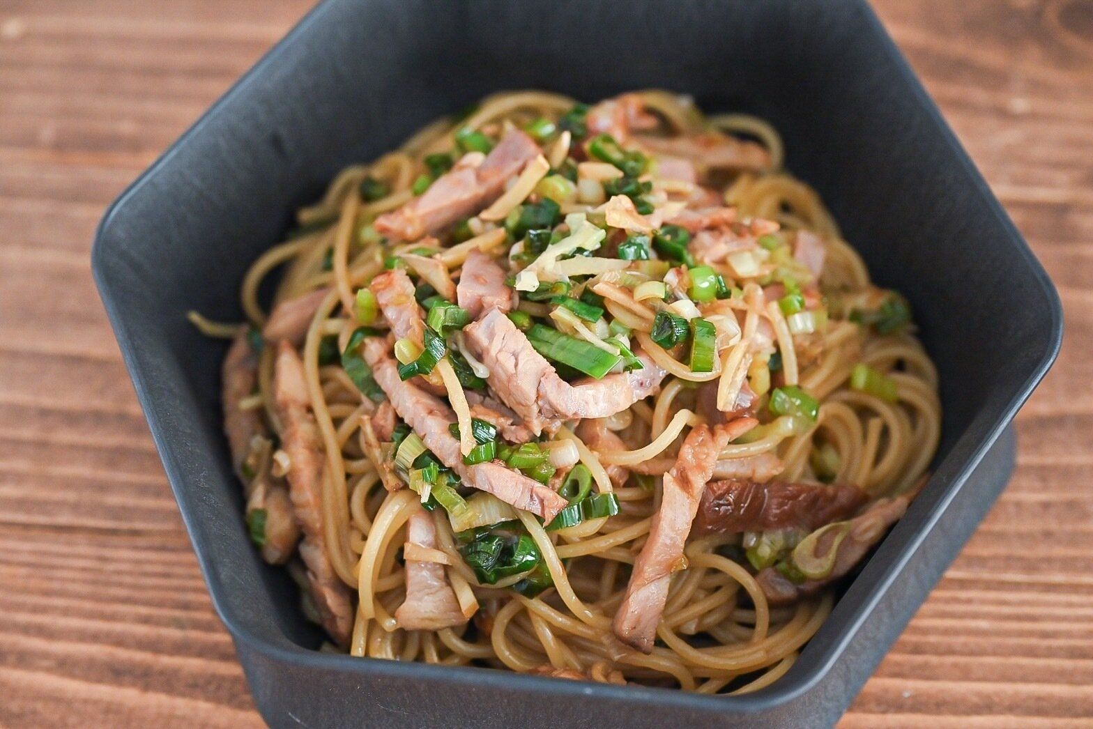 黒い器に入ったチャーシューと長ねぎのパスタ