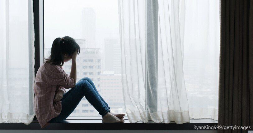 窓辺に座って頭を押さえる女性