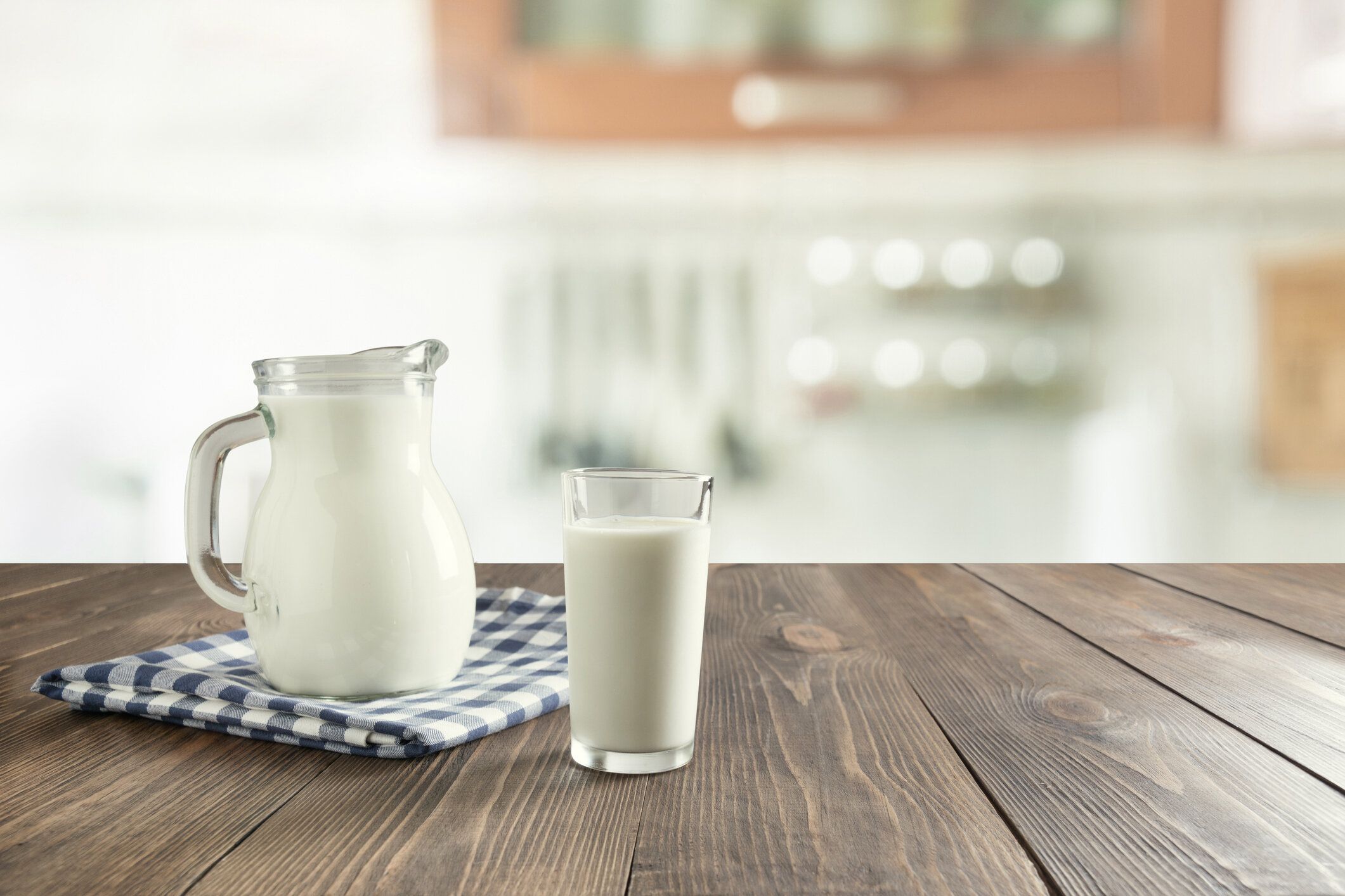 新鮮な牛乳のグラスと背景としてぼかしキッチンと木製の卓上にジャグ。