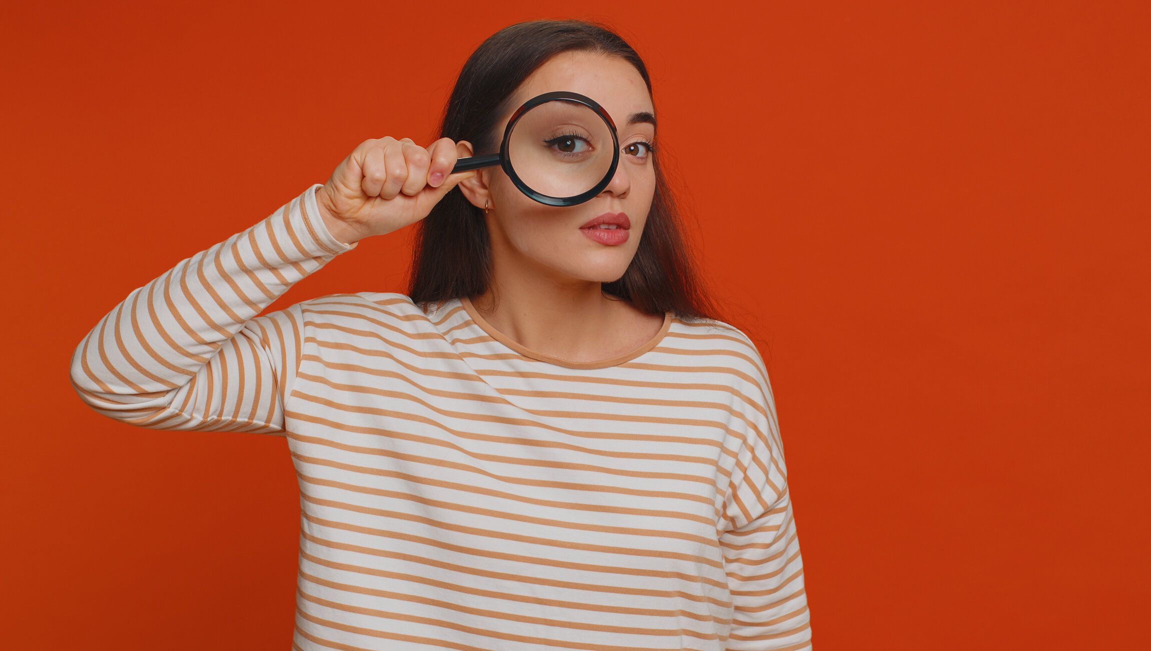 顔の近くに虫眼鏡を持った調査員研究員の女性、大きなズーム目でカメラを覗き込む