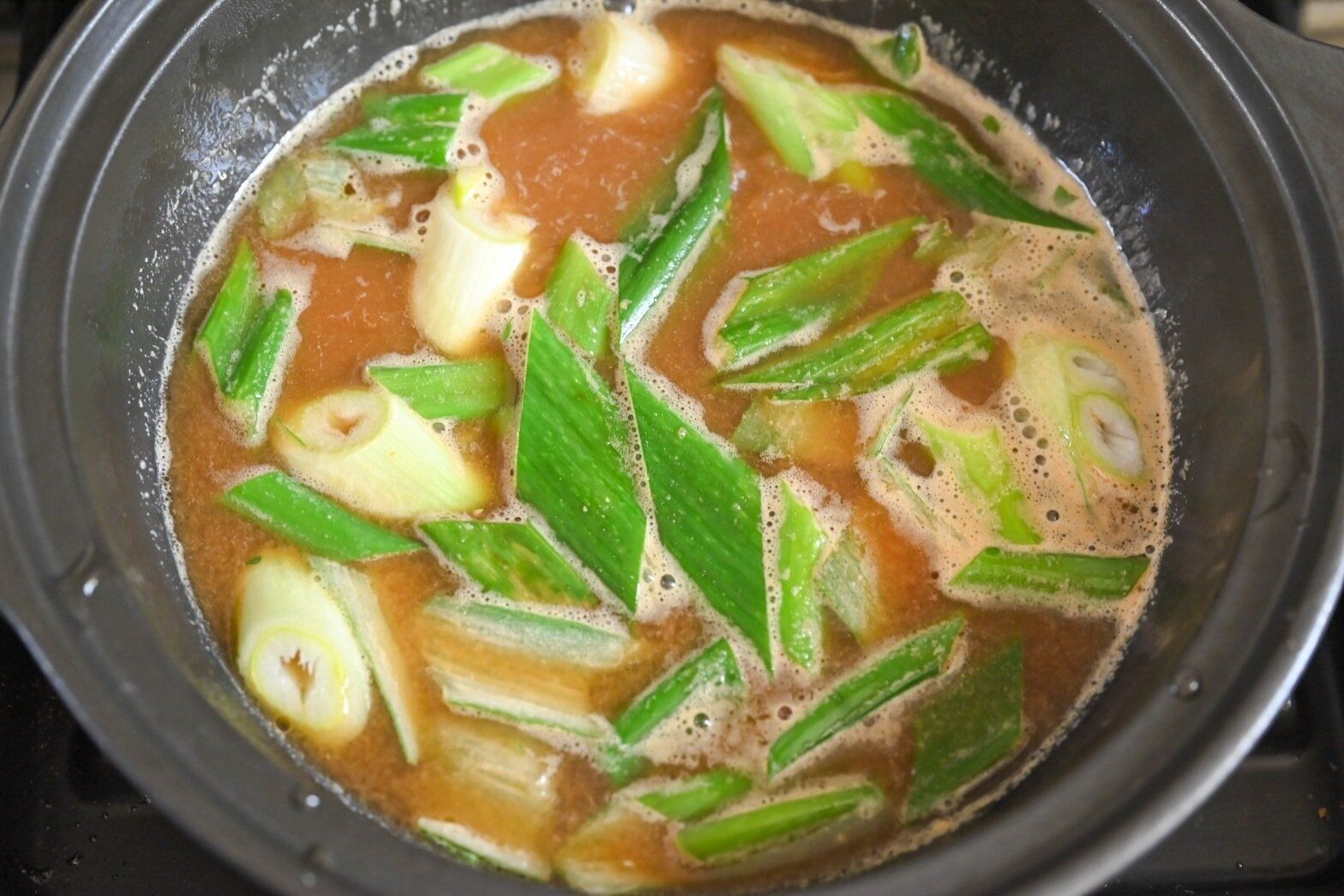 黒い鍋に入った長ねぎ入りの海老だし味噌鍋