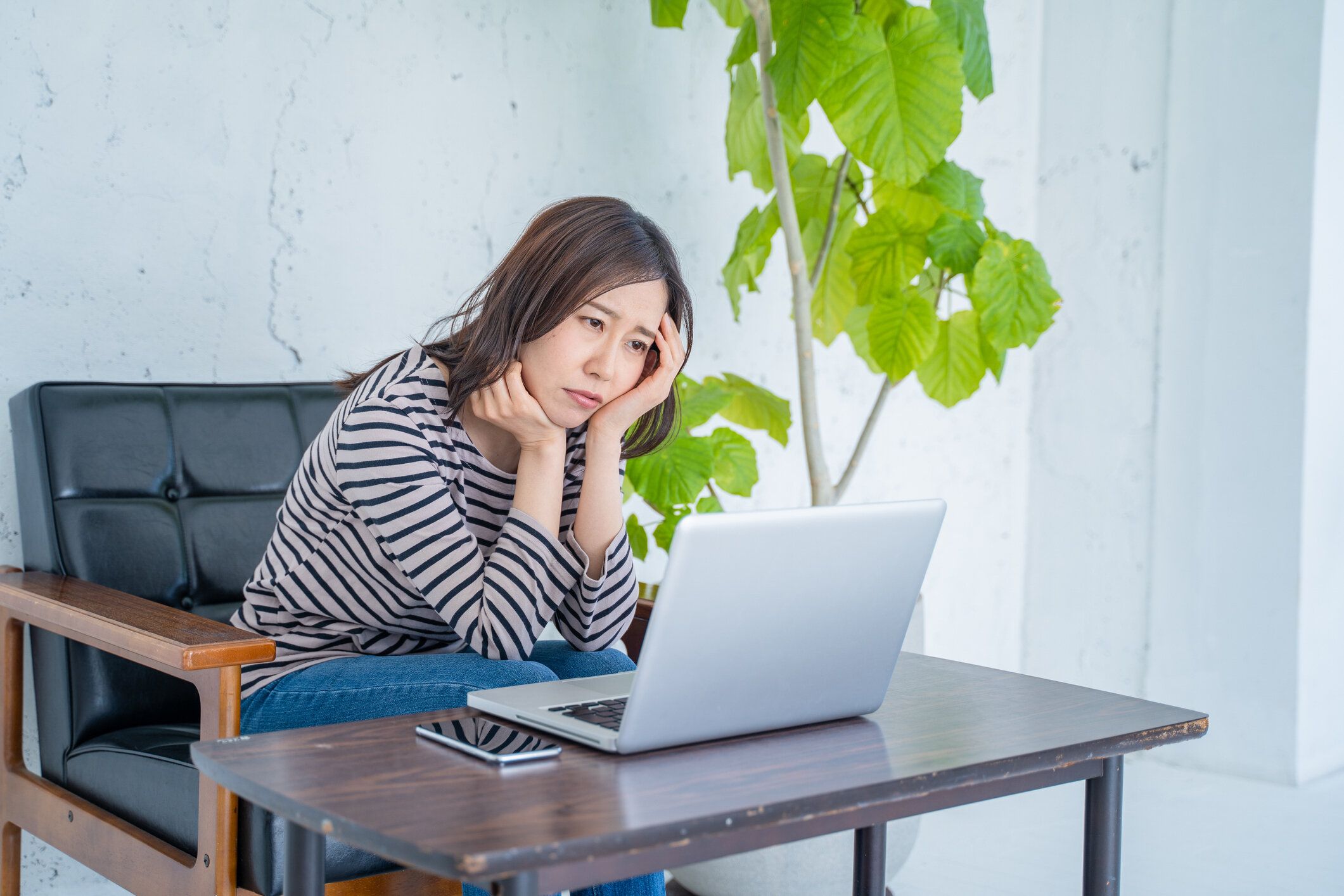 居間で頭を抱えてコンピューターで作業する女性。