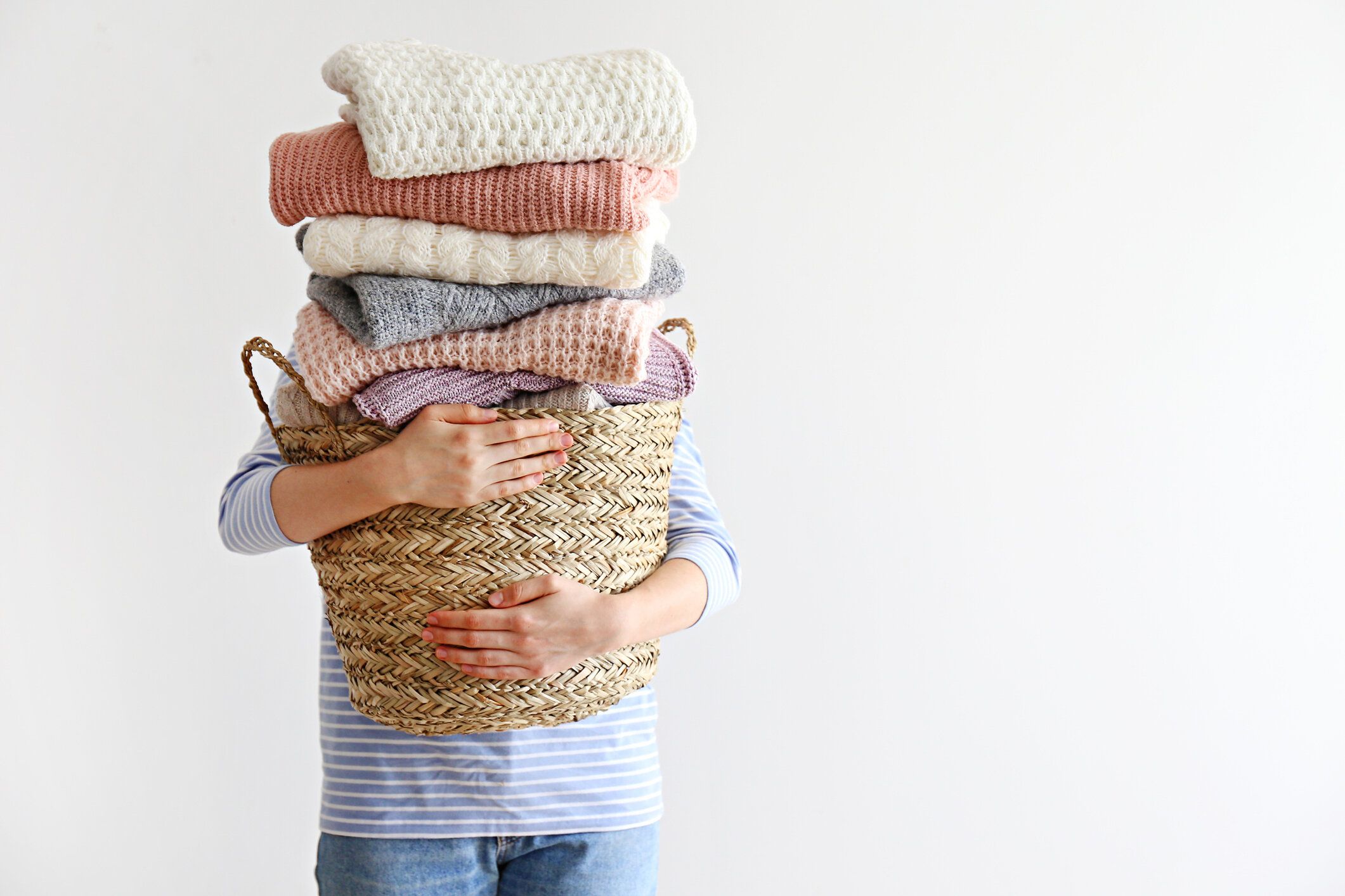 女性の手に完全に積み重ねられた異なる色やパターンのニットセーターの山。