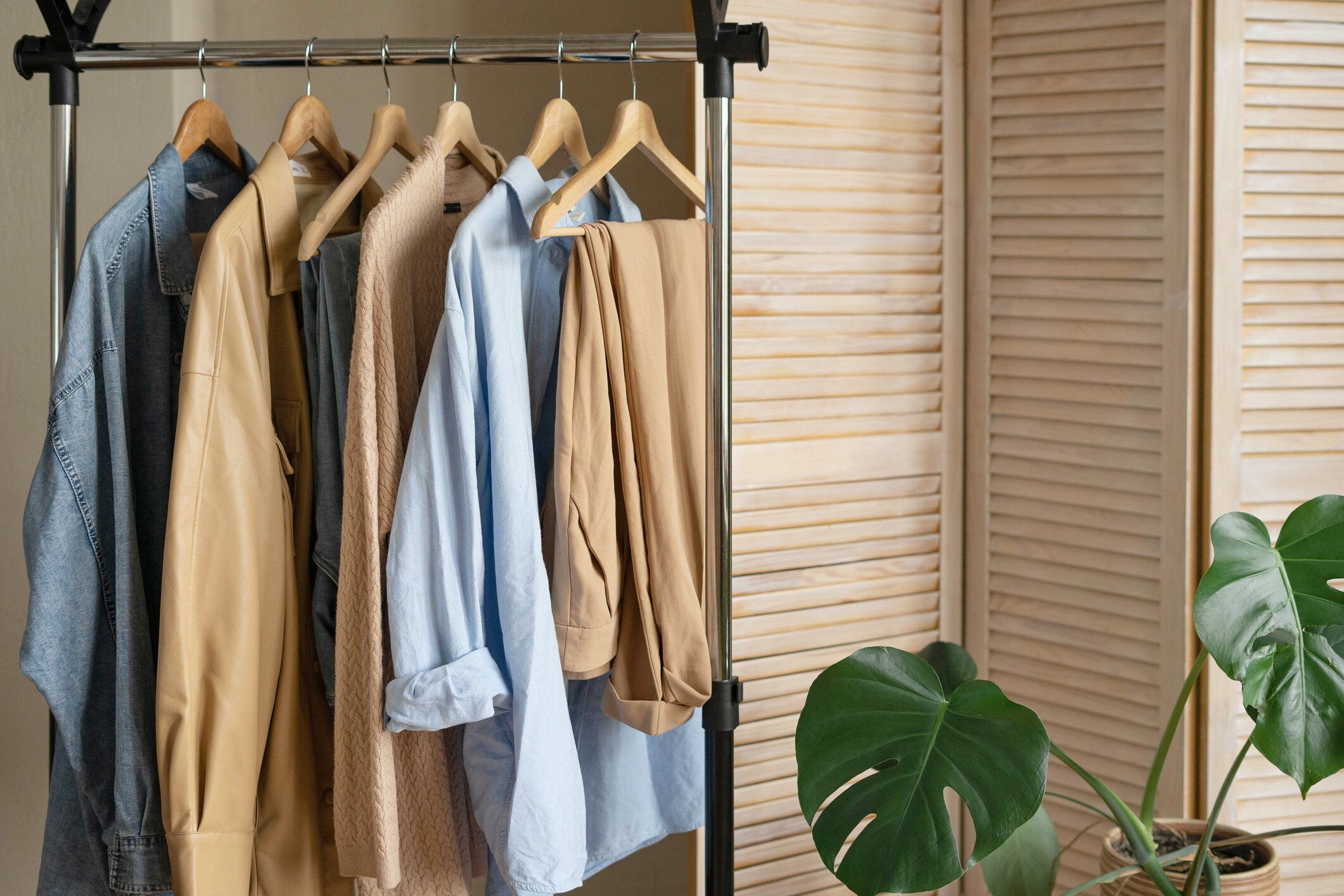 ベージュと水色のトレンディなカプセルワードローブは、スクリーンを背景にしたレールラックに取り付けられています。