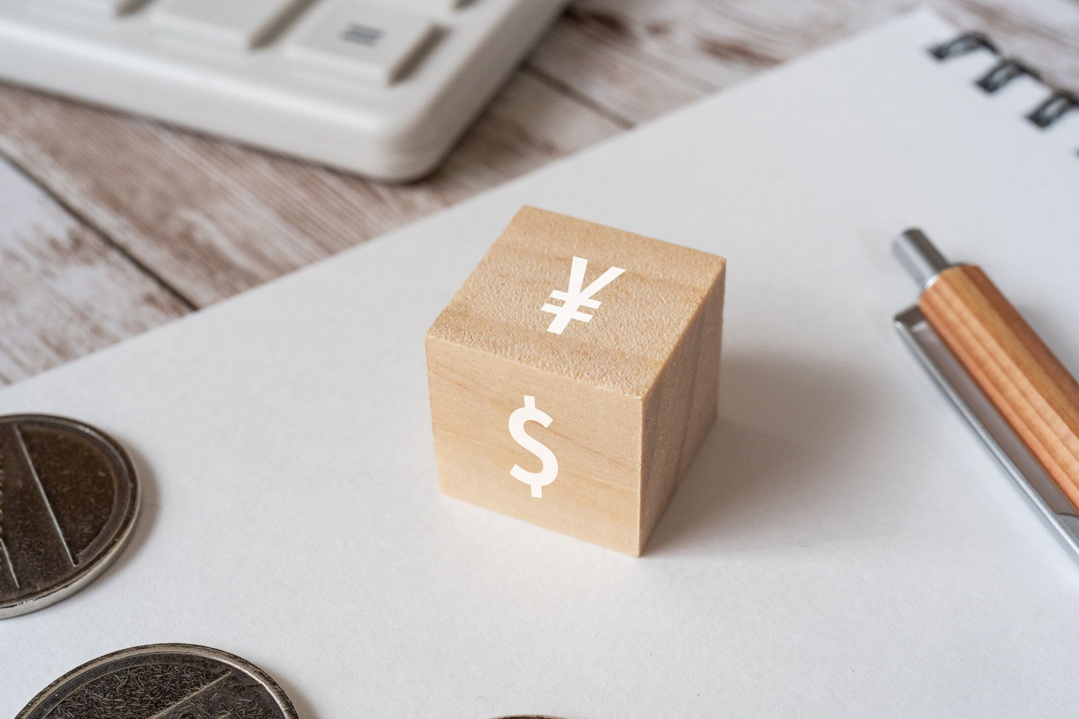 ドルと円記号、ペン、ノート、コイン、電卓を持つ木製のブロック。