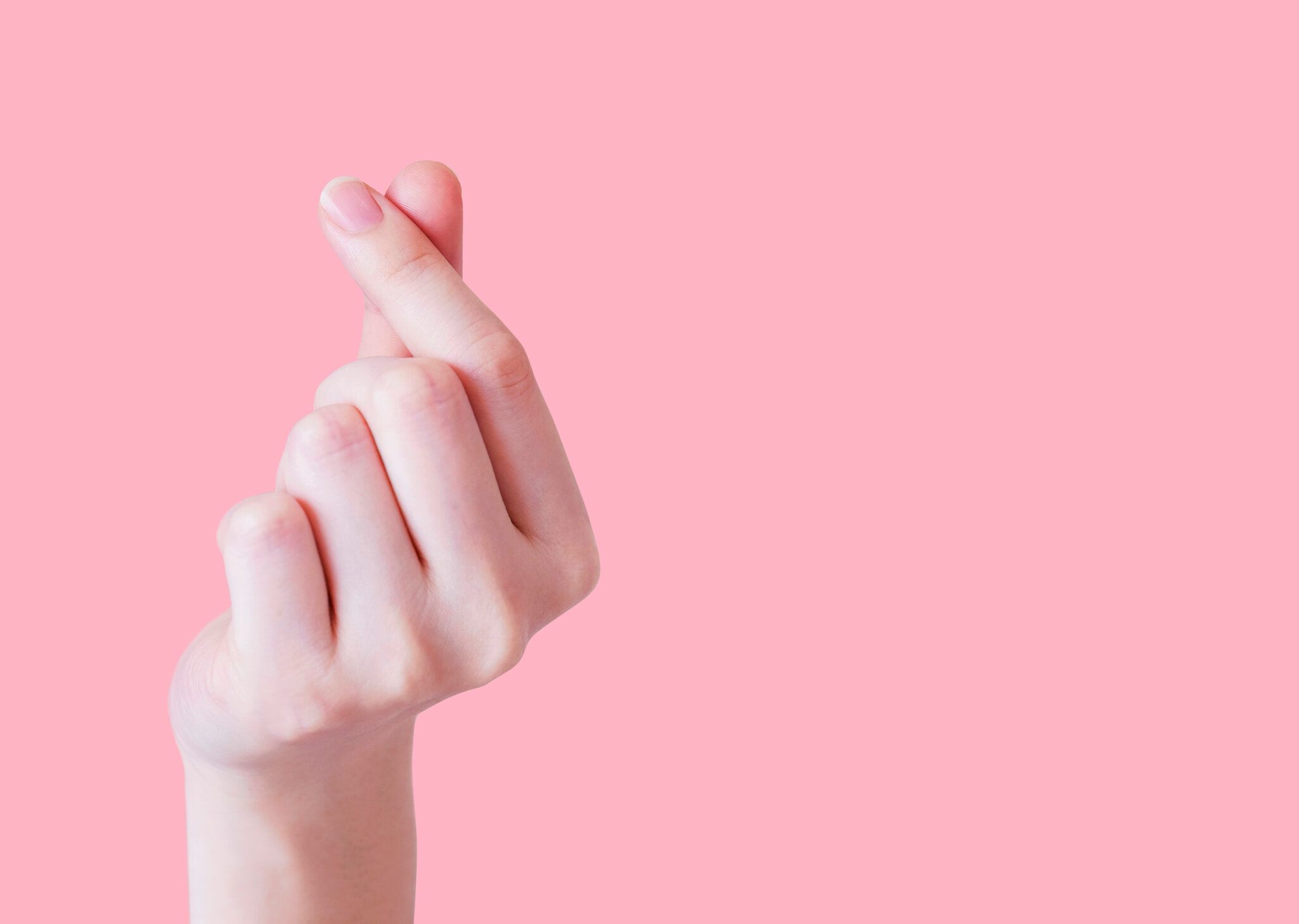 コピースペースでピンクの背景にミニハートを作る若い女性の手の愛の概念