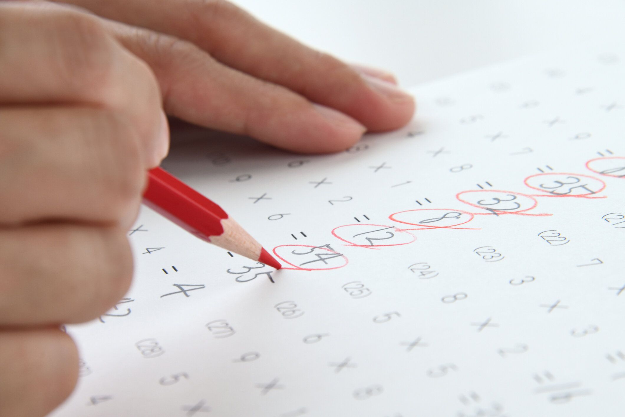 赤鉛筆で数学のテストシートをチェックするティーサーの手