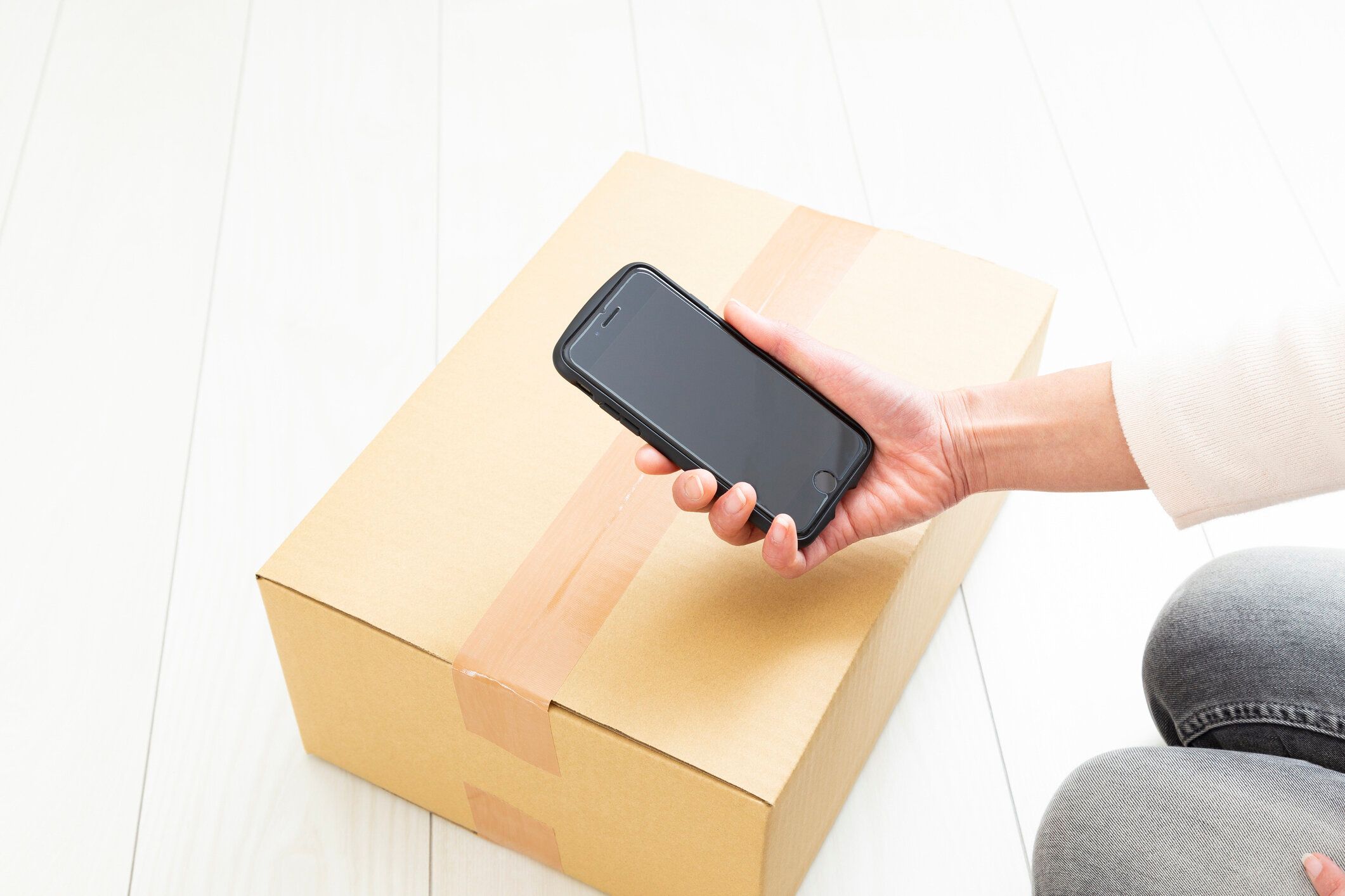 女性の手がスマートフォンで箱の写真を撮る。