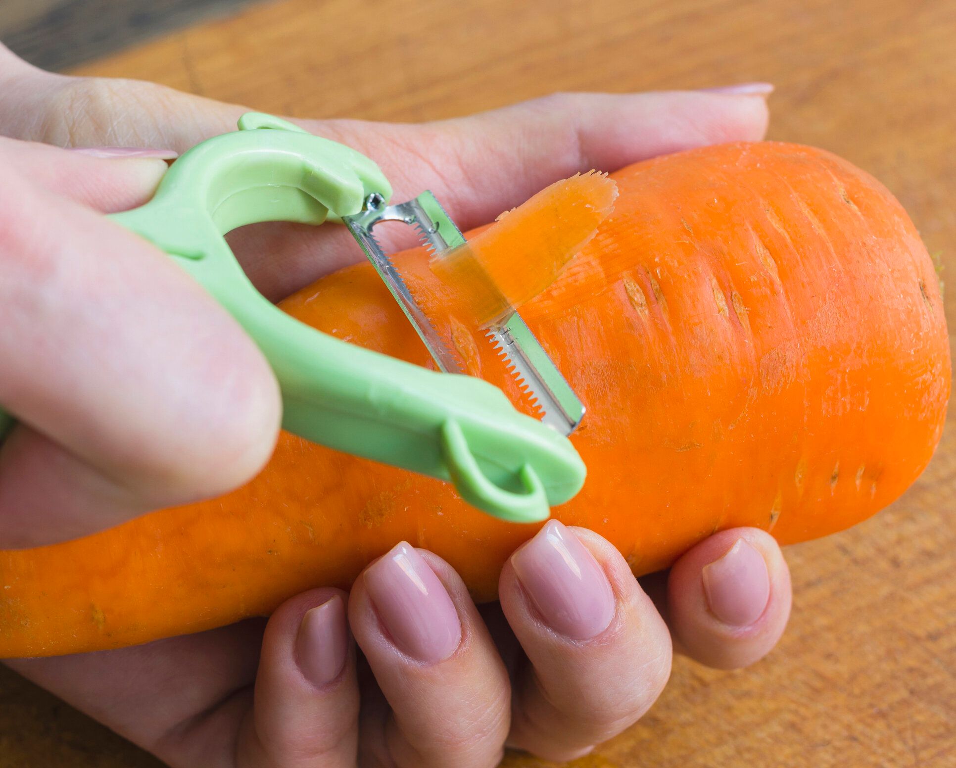 女性は、野菜の皮むき器と新鮮なニンジンから皮膚を削除します。健康的な食事。選択と集中。