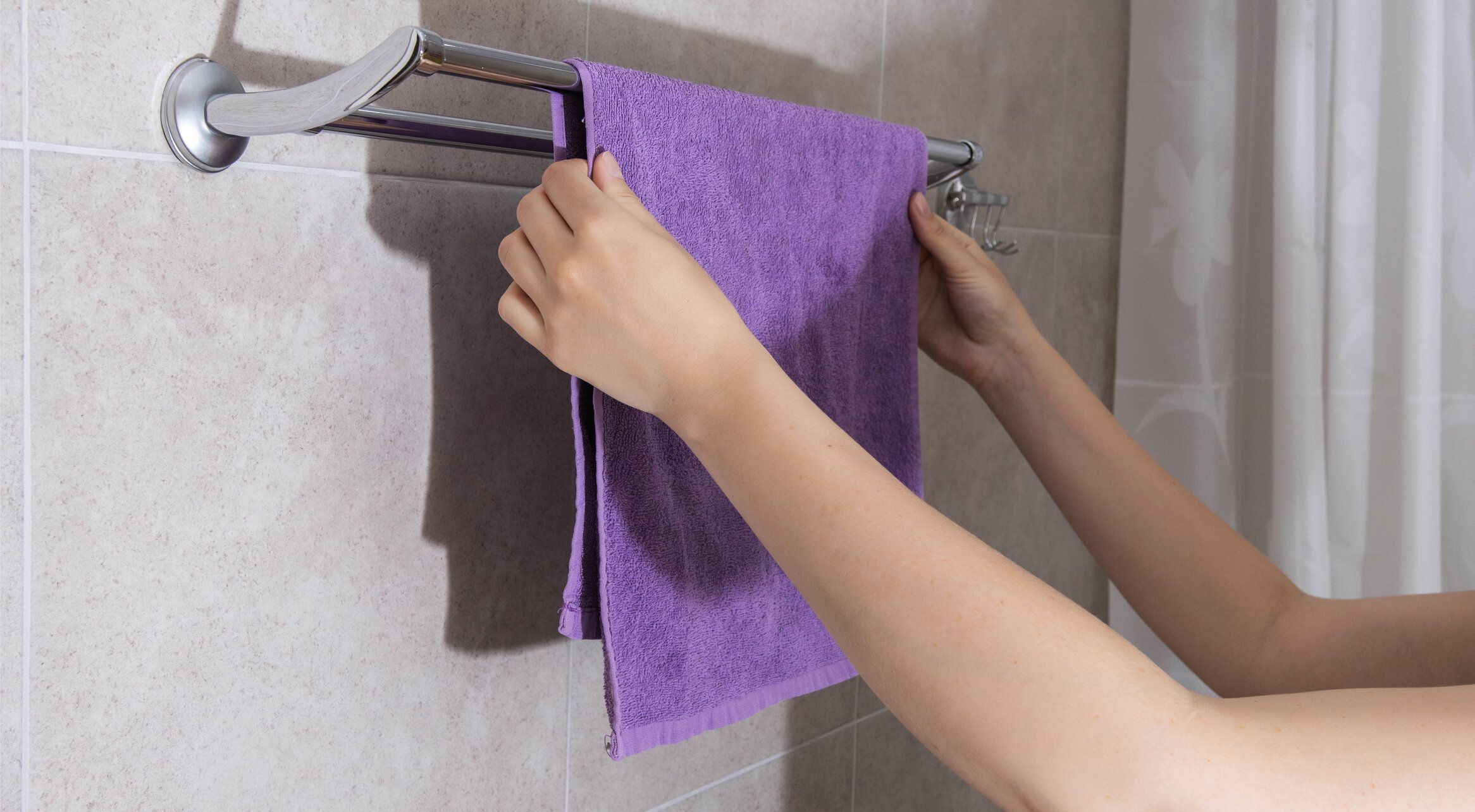女の子がバスルームの壁掛けに薄紫色のタオルを掛けて乾かし、接写する