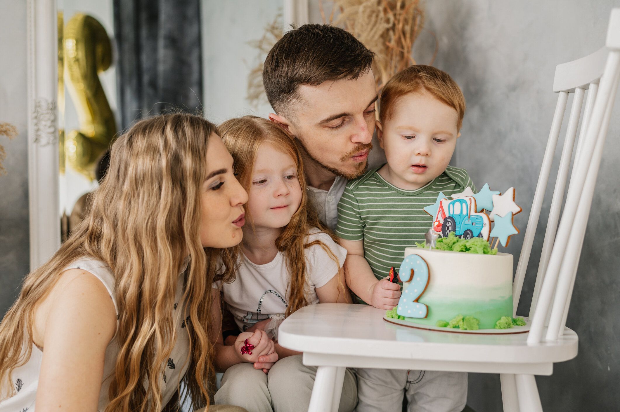 子供を抱きしめる母、父。誕生日レセプション。お母さん、お父さん、娘はスタジオで誕生日に息子を祝福します。幸せな家族はケーキを持ち、ろうそくを吹き、2年の誕生日パーティーを楽