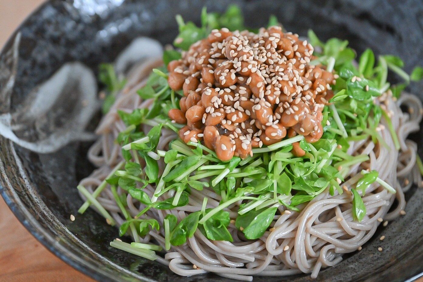 黒い皿に盛られた納豆と豆苗のそば