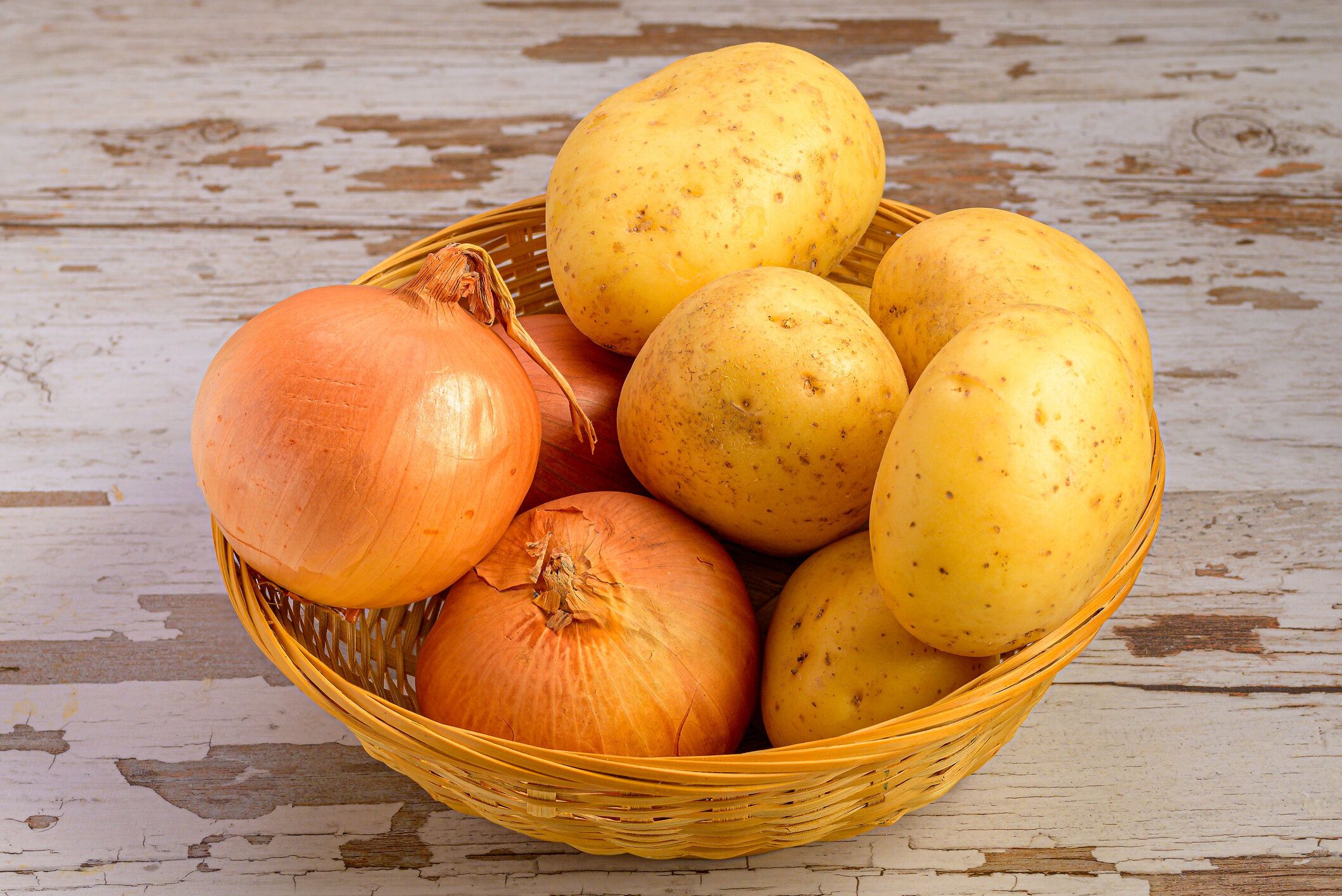 木の表面の枝編み細工品バスケットに入ったジャガイモと玉ねぎの接写