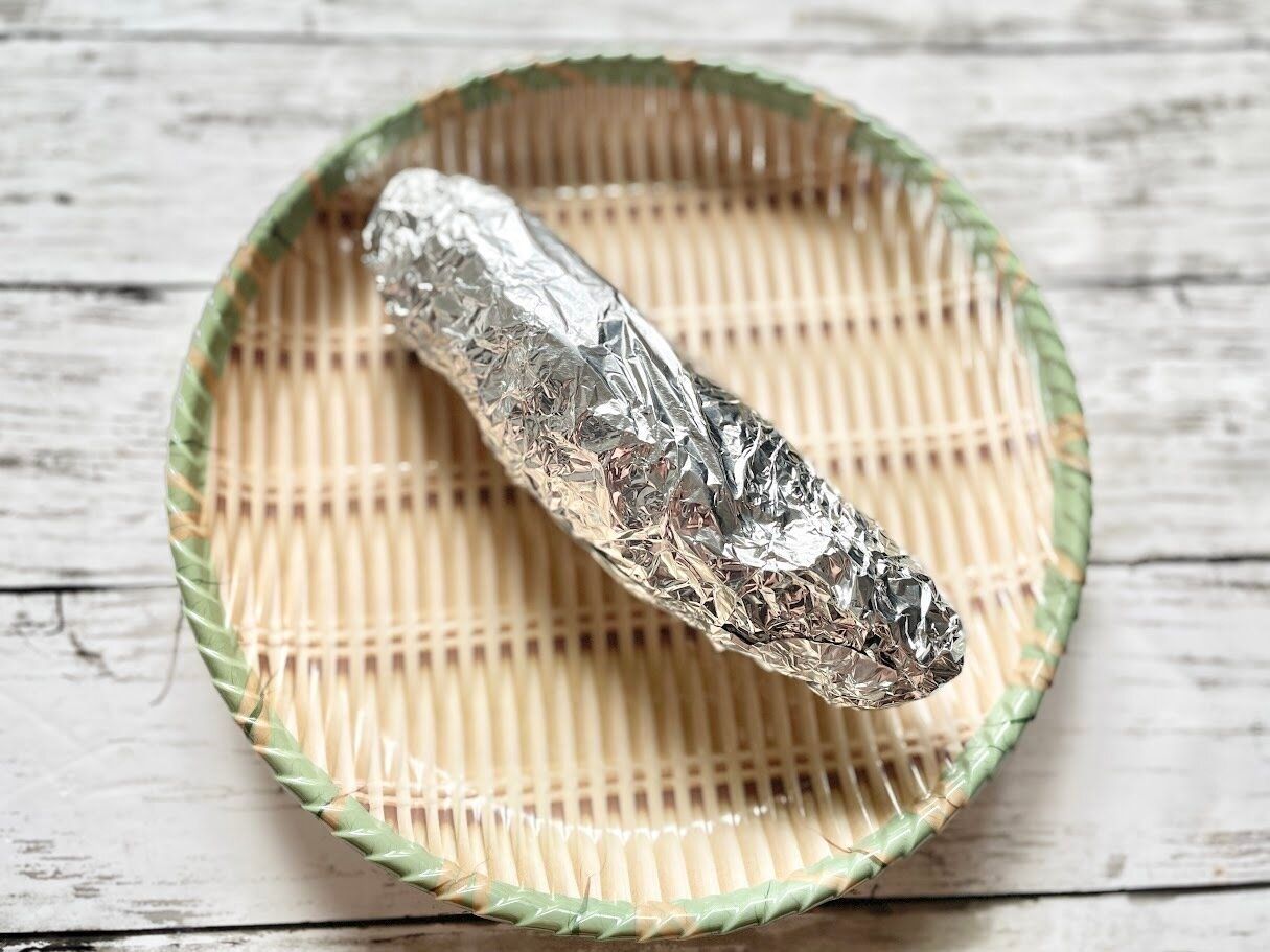 新聞紙に包んださつまいもを、さらにアルミホイルで包む