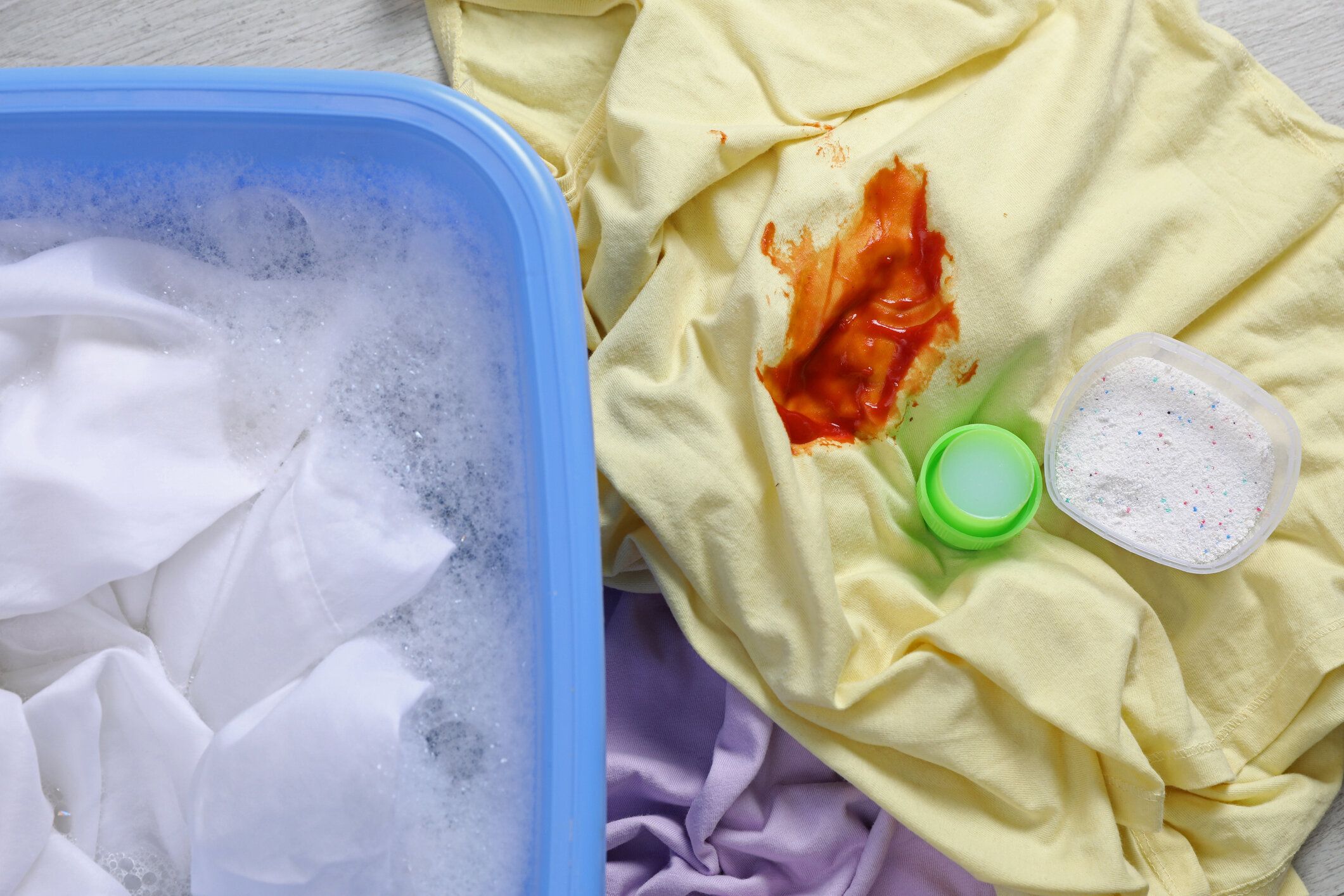 白いシャツを着た洗面器の近くに汚れた衣服と洗剤、上面図。手洗い洗濯物