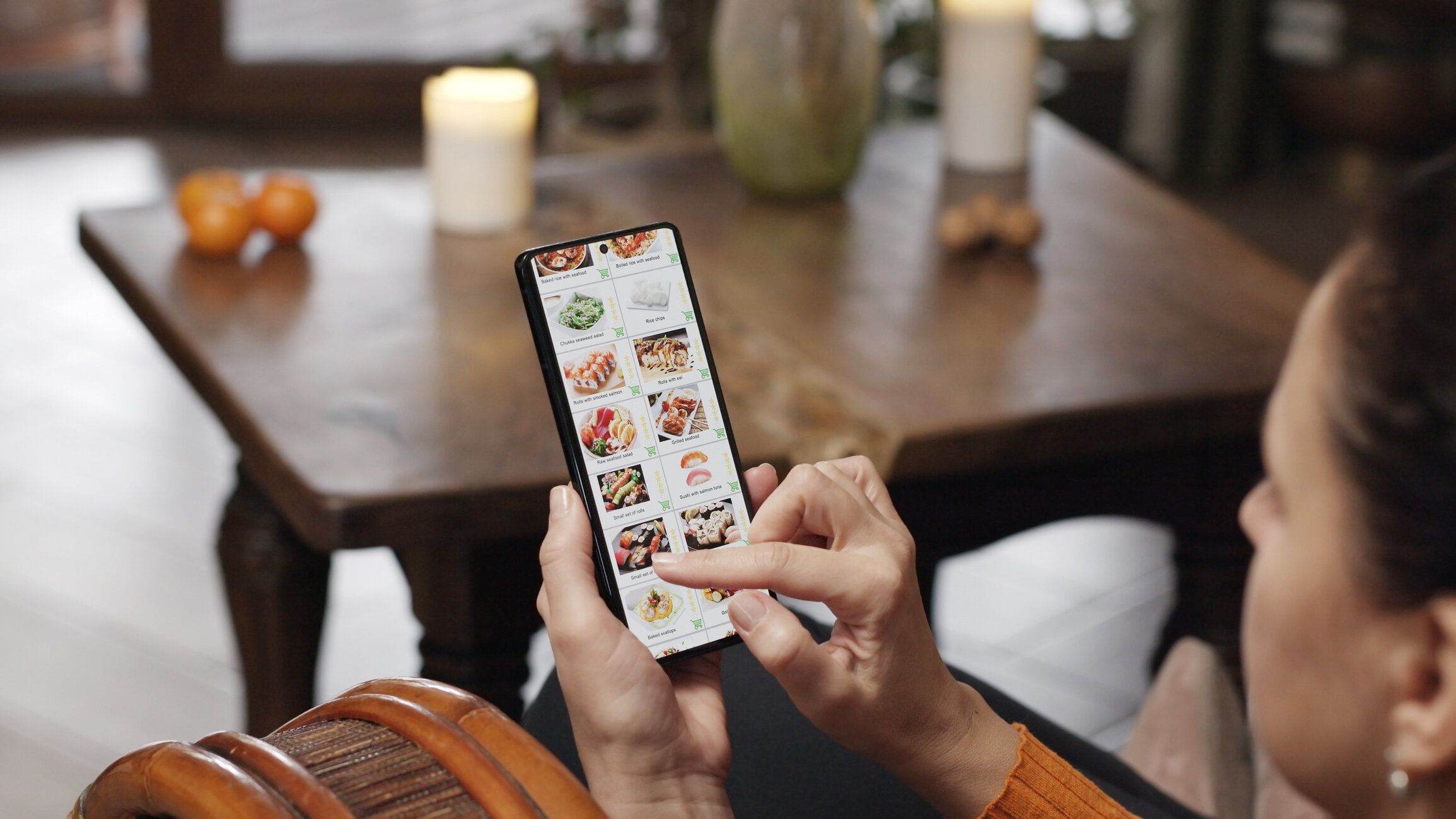 自宅でスマートフォンを使って食べ物を注文する。女性がスマートフォンのアプリを使って日本食レストランのインターネットメニューで寿司セットを選ぶ。暖炉の中で燃えている火のある�