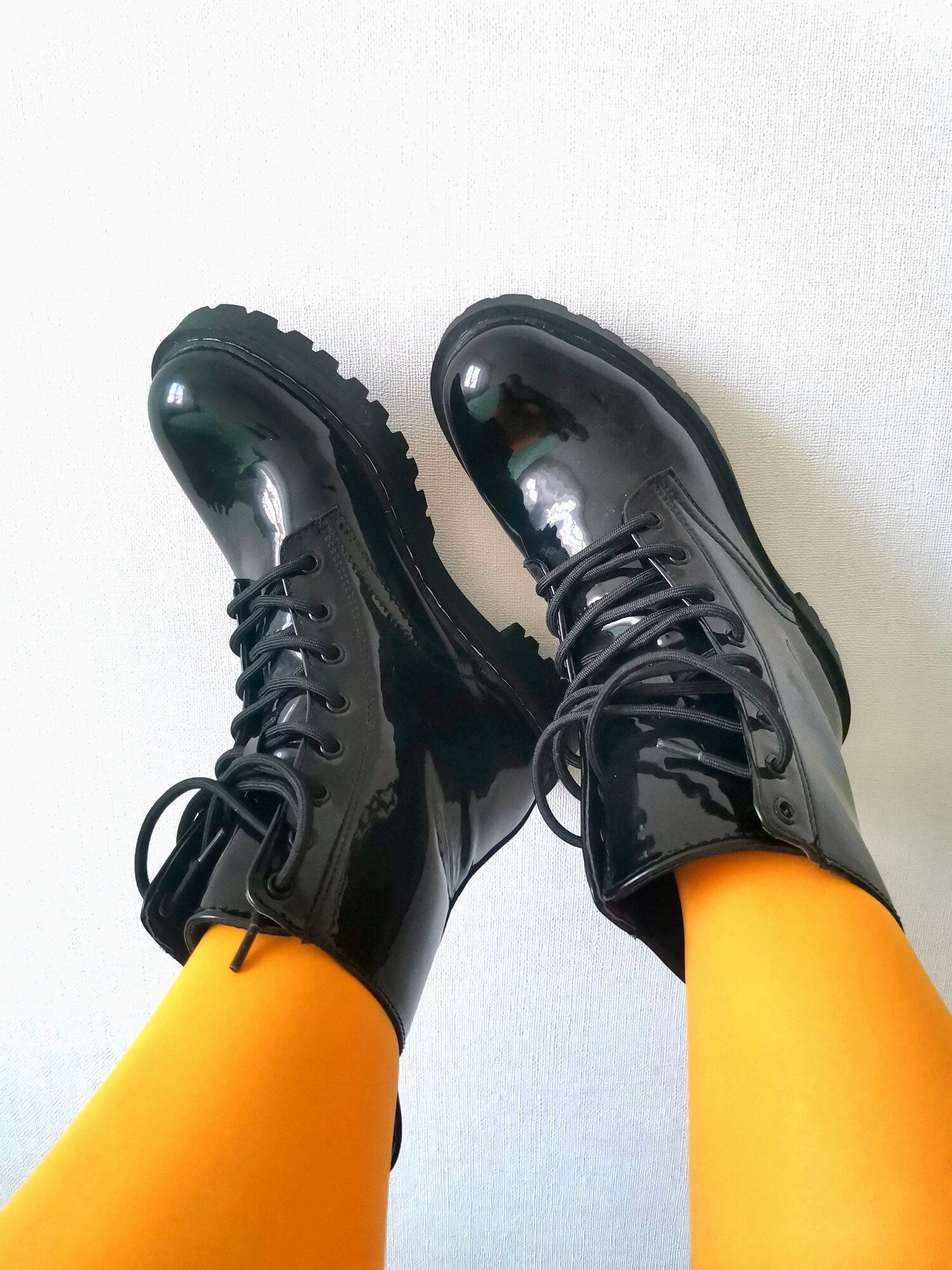 白い背景に、黄色いタイツと黒いレースアップブーツの男性の脚