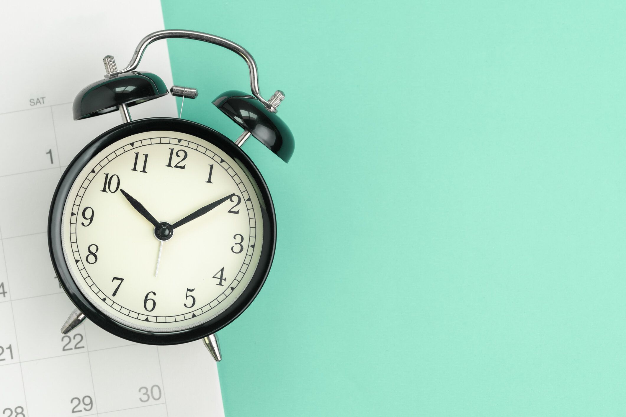 コピースペース、休暇のスケジュール、ビジネスの予定やビジネスプロジェクトの締め切りにリマインダーとパステルグリーンの背景に白いカレンダーと黒の目覚まし時計のフラットまたは�