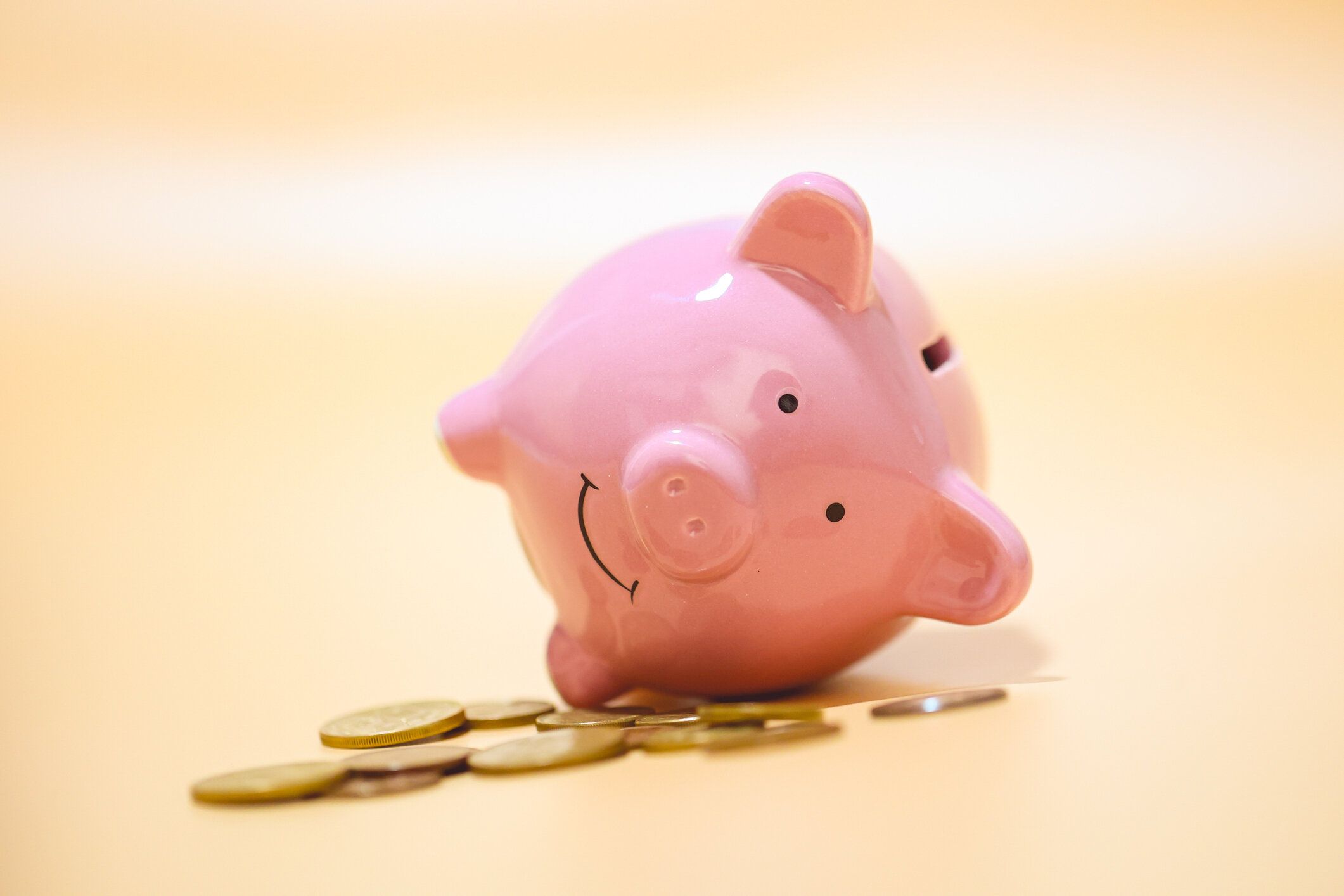 スタジオショットでコインを持って横たわっている貯金箱。オレンジ色の背景。