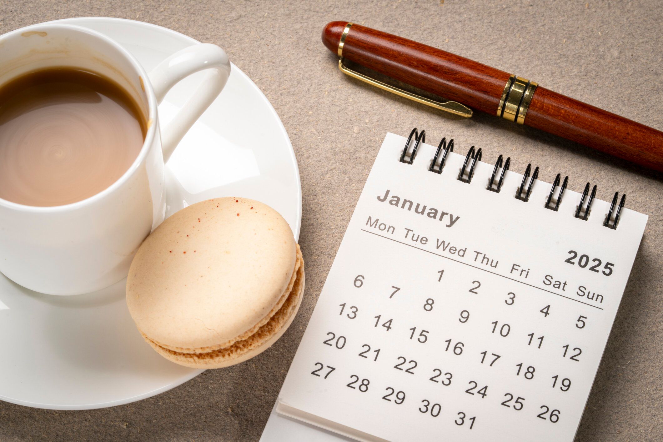 2025年1月 - スタイリッシュなペンと一杯のコーヒー、時間、ビジネスコンセプトを備えた小さなスパイラルデスクトップカレンダー