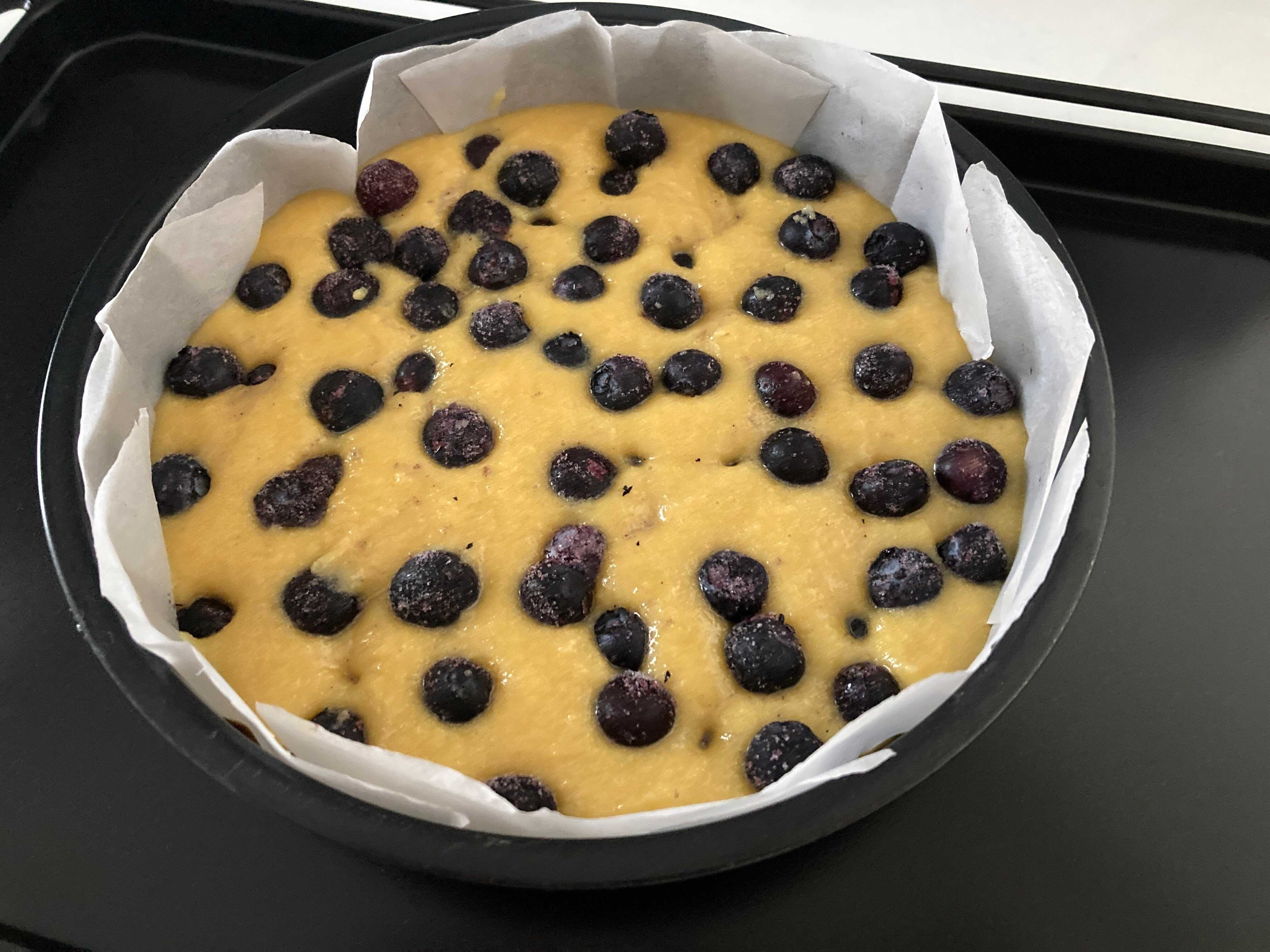 ケーキの生地を型に流し入れ、冷凍ブルーベリーをトッピングしている