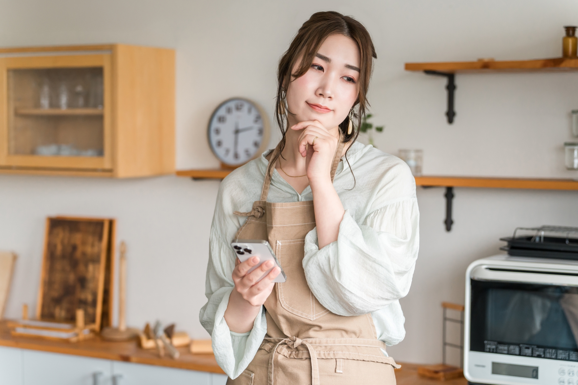 キッチンでスマホ持って考えている女性