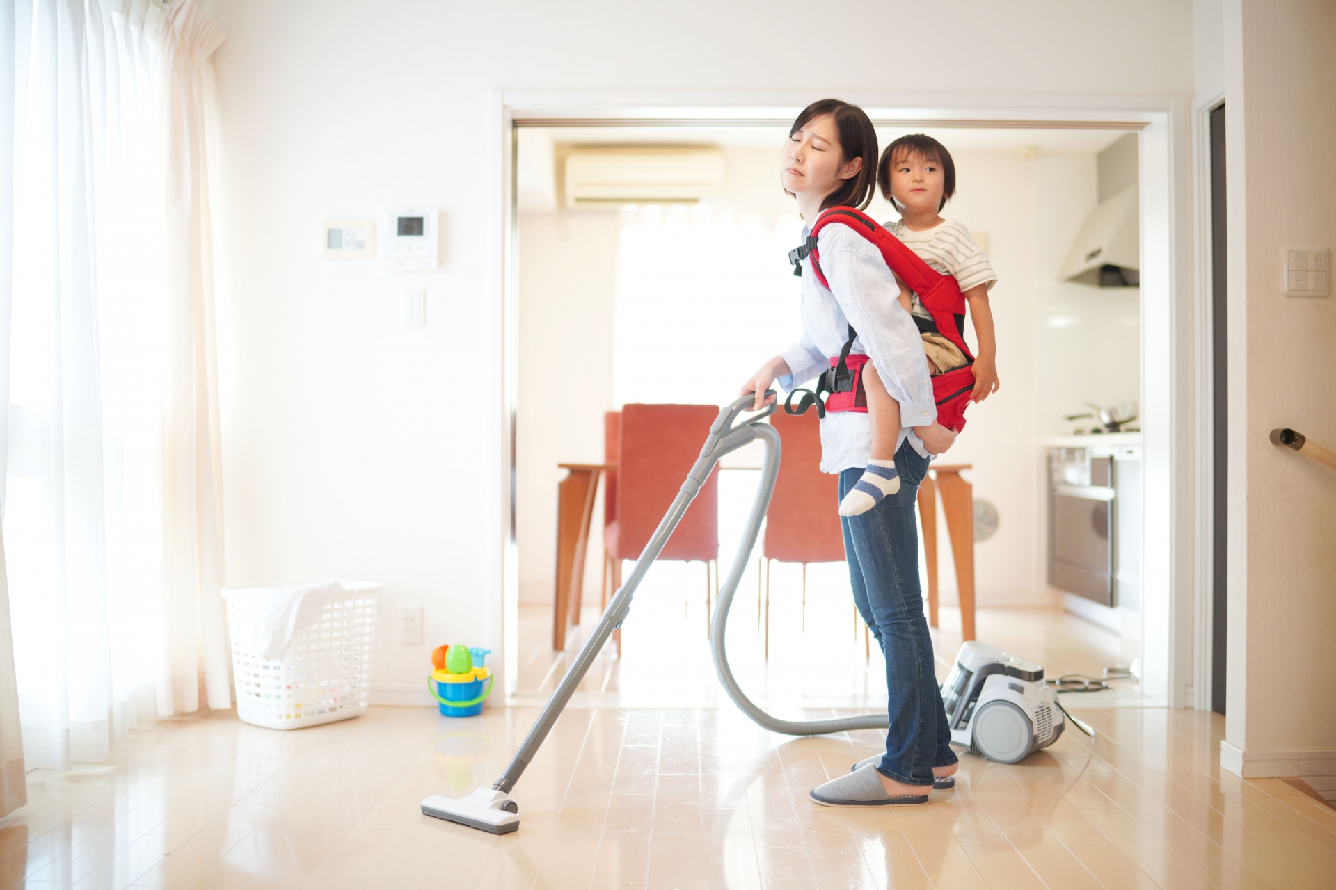 子供をおんぶしながら掃除機をかけるお母さん