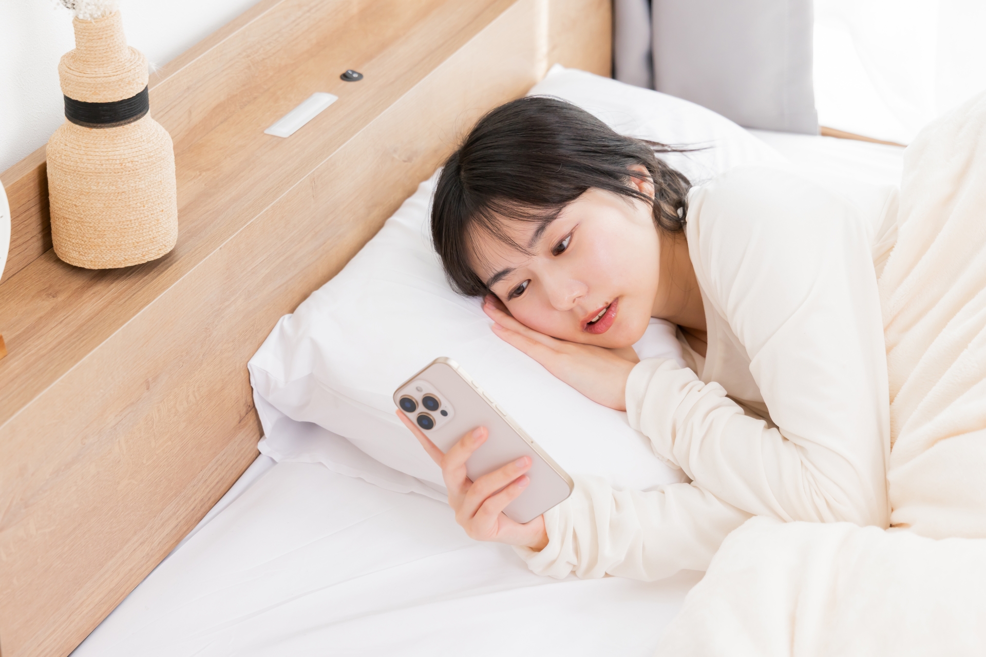 ベッドの中でスマホを見る女性