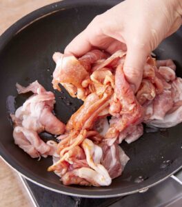 フライパンに入れた豚肉に、しょうゆをふってなじませている様子