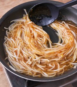 フライパンにもやしを入れて炒め、合わせ調味料をよく混ぜて片栗粉を溶かしてから加え、煮ている様子