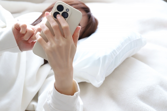 寝転びながらスマホを操作する女性