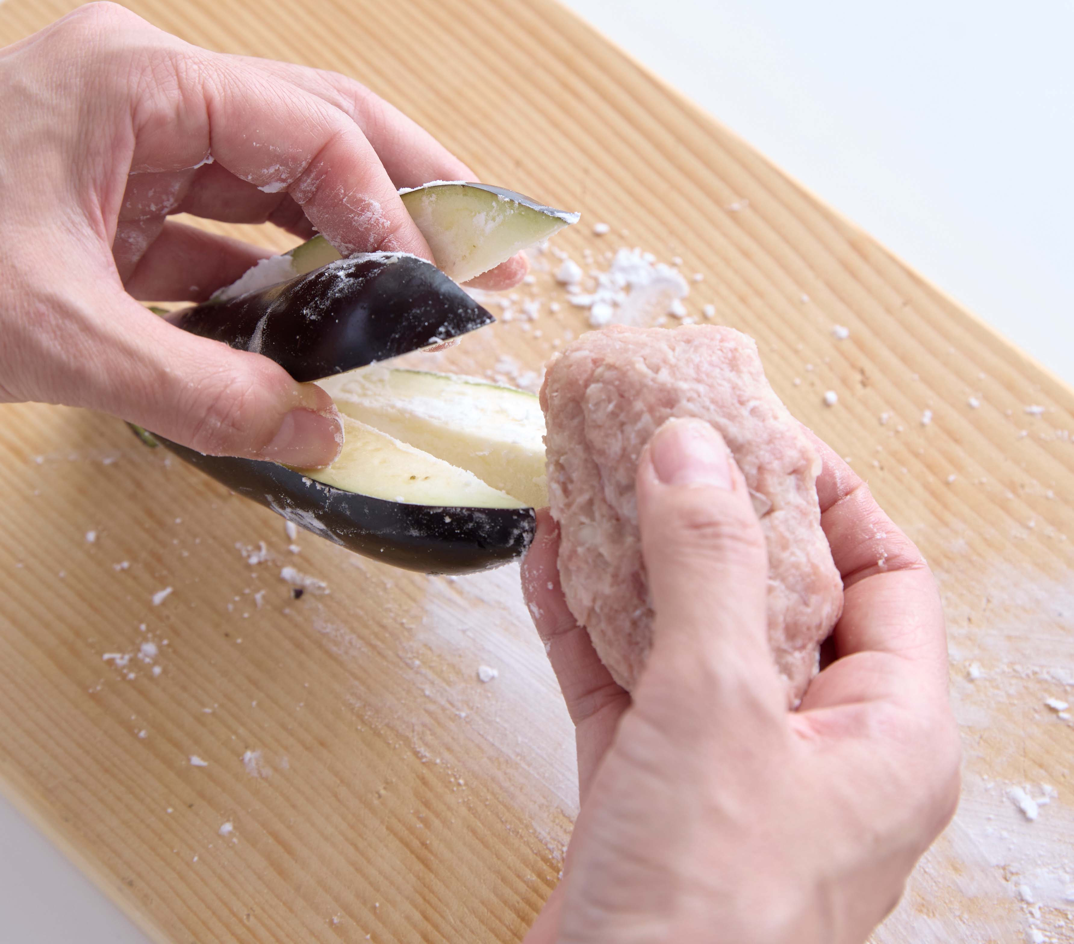 ひき肉だねをたわら形にまとめ、片栗粉を塗ったなすの切り込みの間に詰めている様子