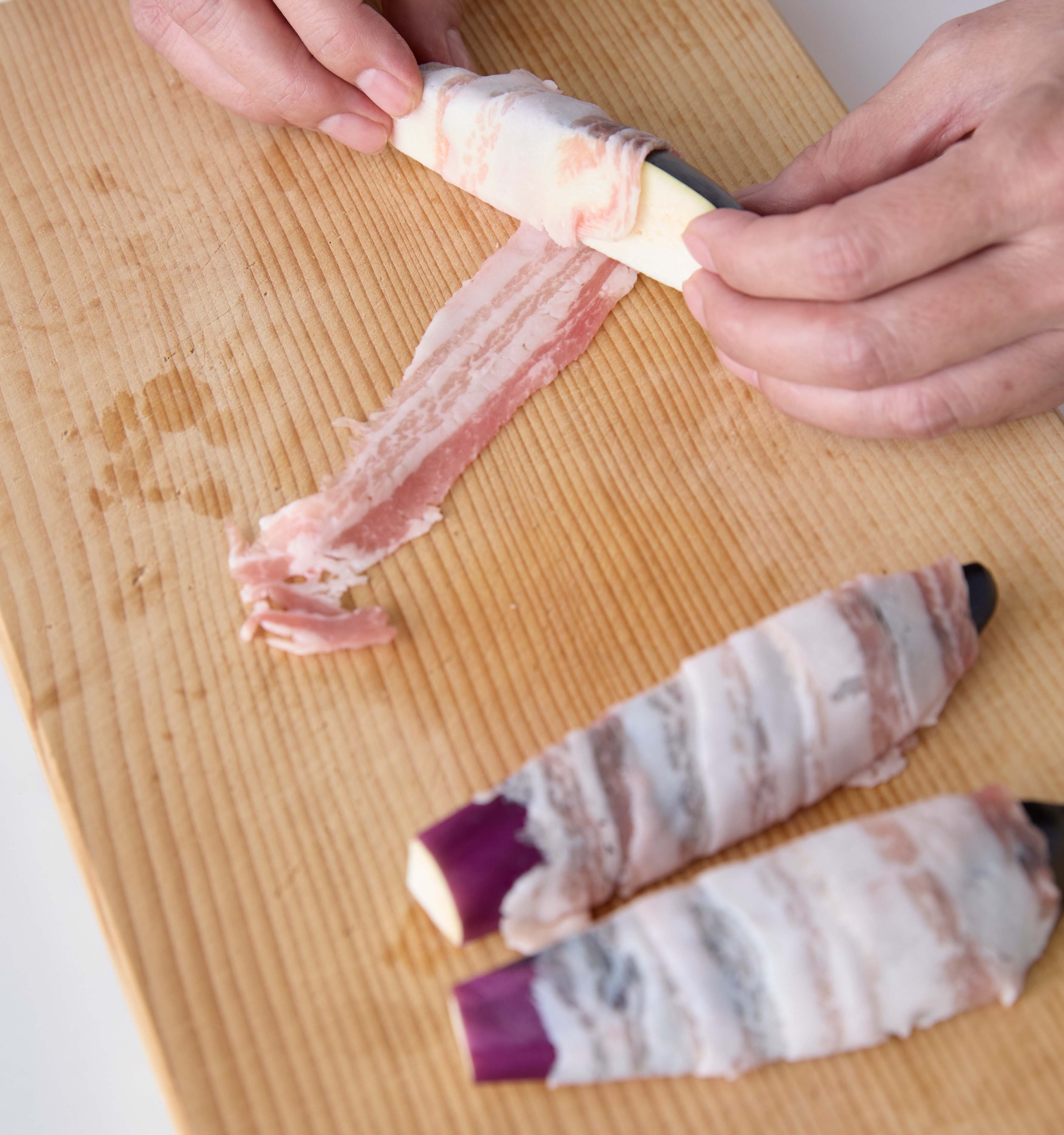 豚肉を広げた手前になすを斜めに置いてらせん状にきつめに巻きつけている様子